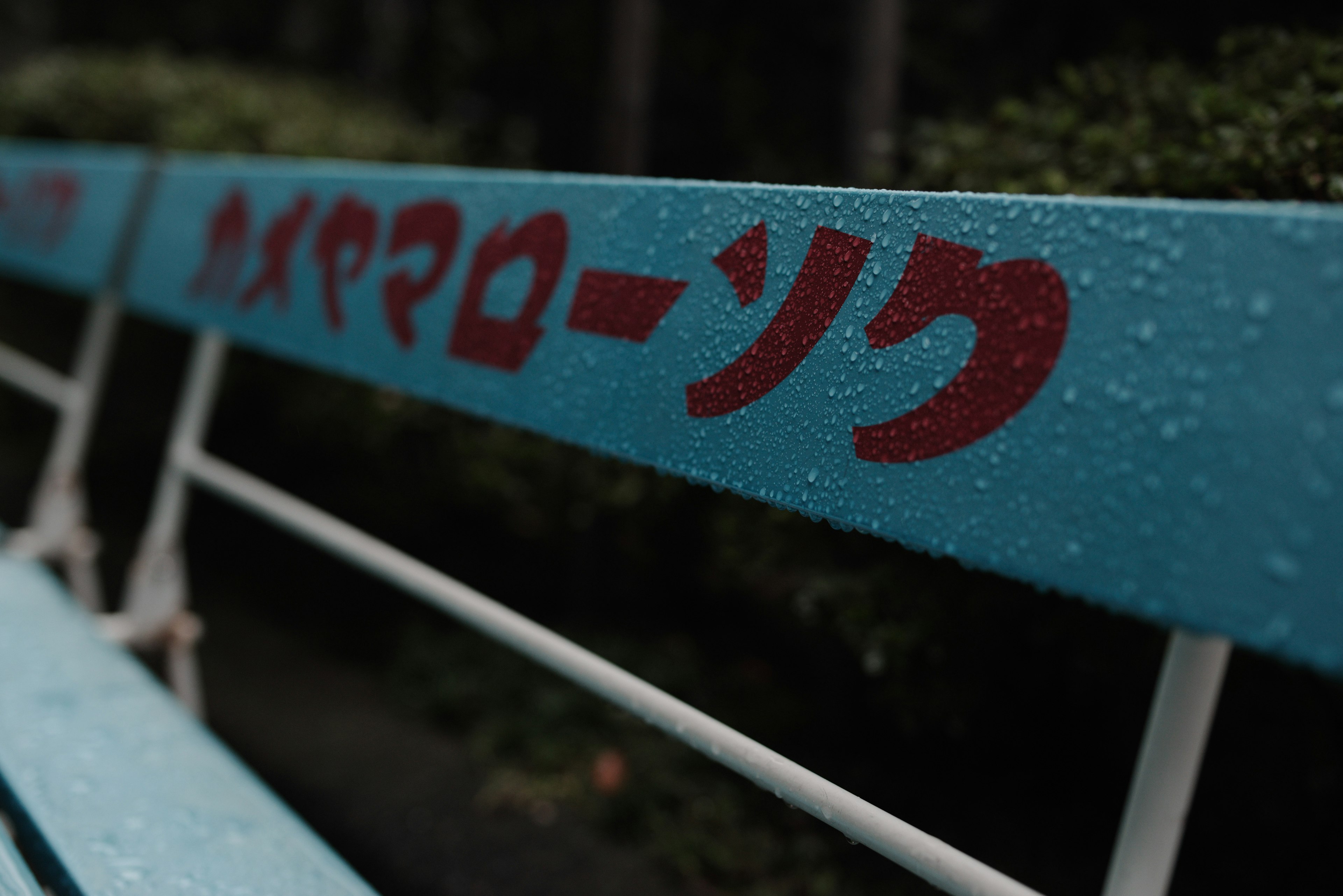 Blue bench with katakana text wet from rain