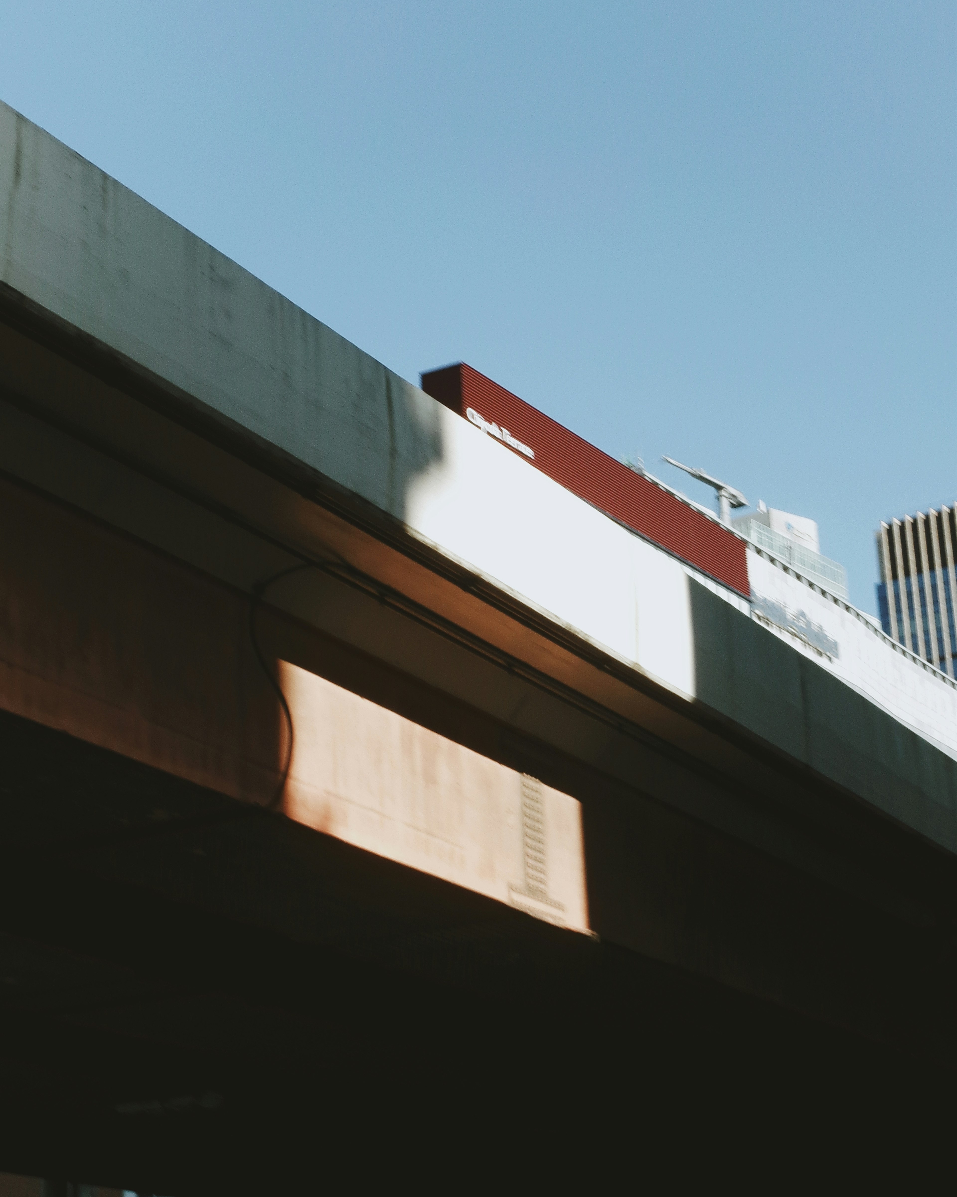 Parte de una carretera elevada bajo un cielo azul con sombras de edificios