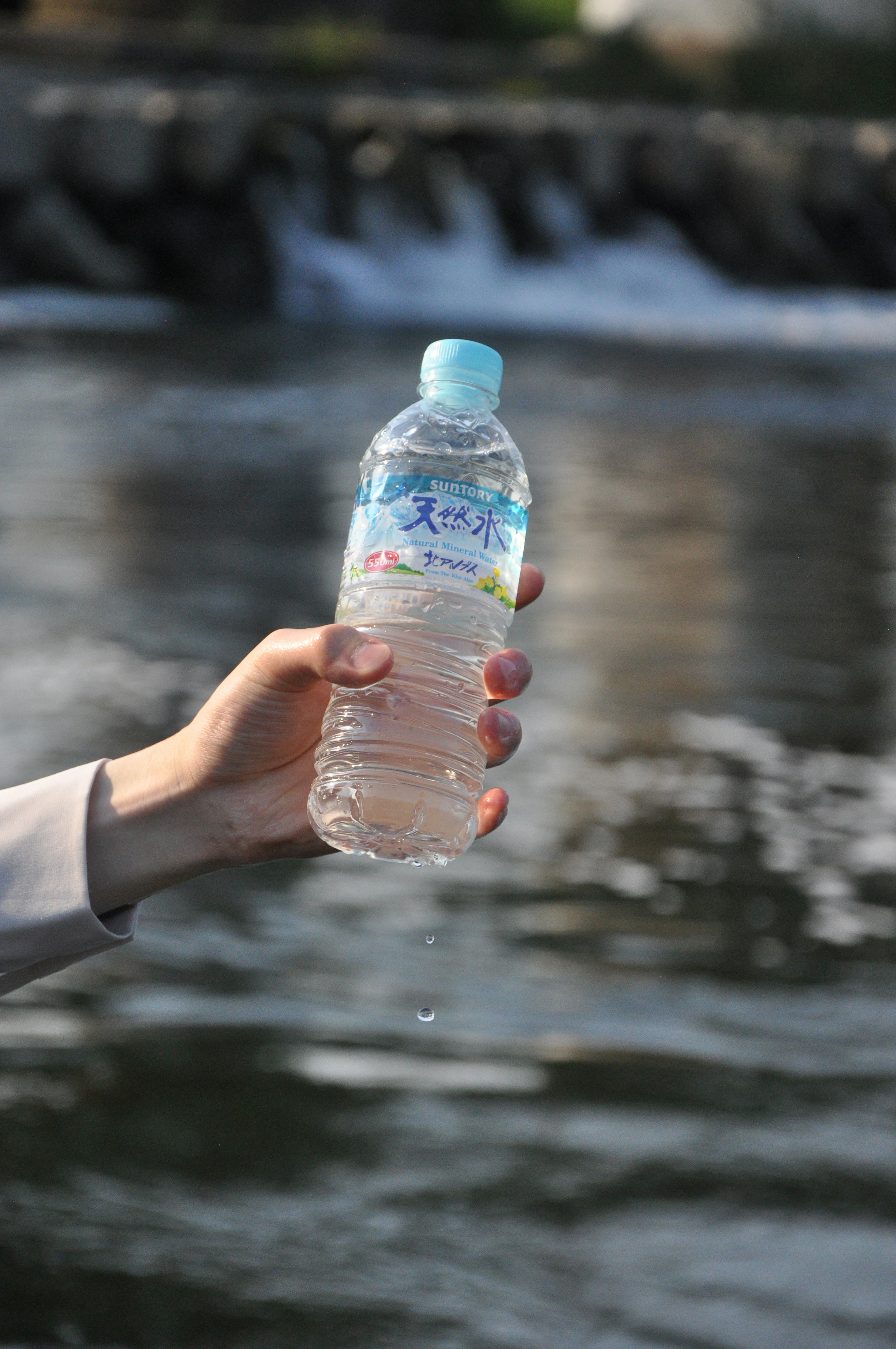 Hand holding a water bottle with a blurred water background