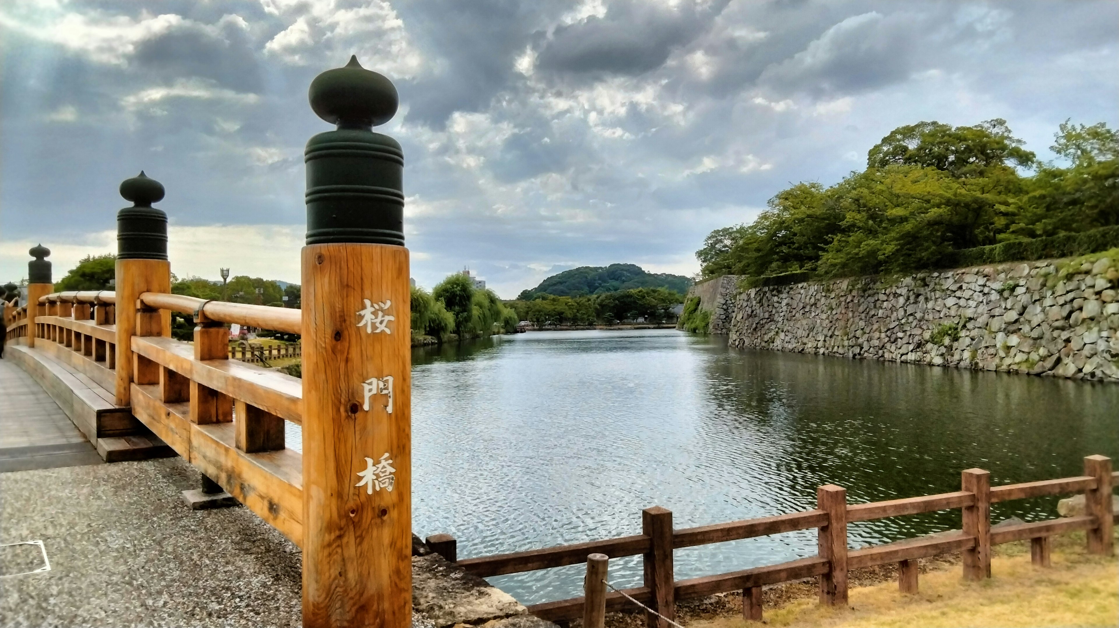 Vista escénica junto al río con un puente de madera y un muro de piedra