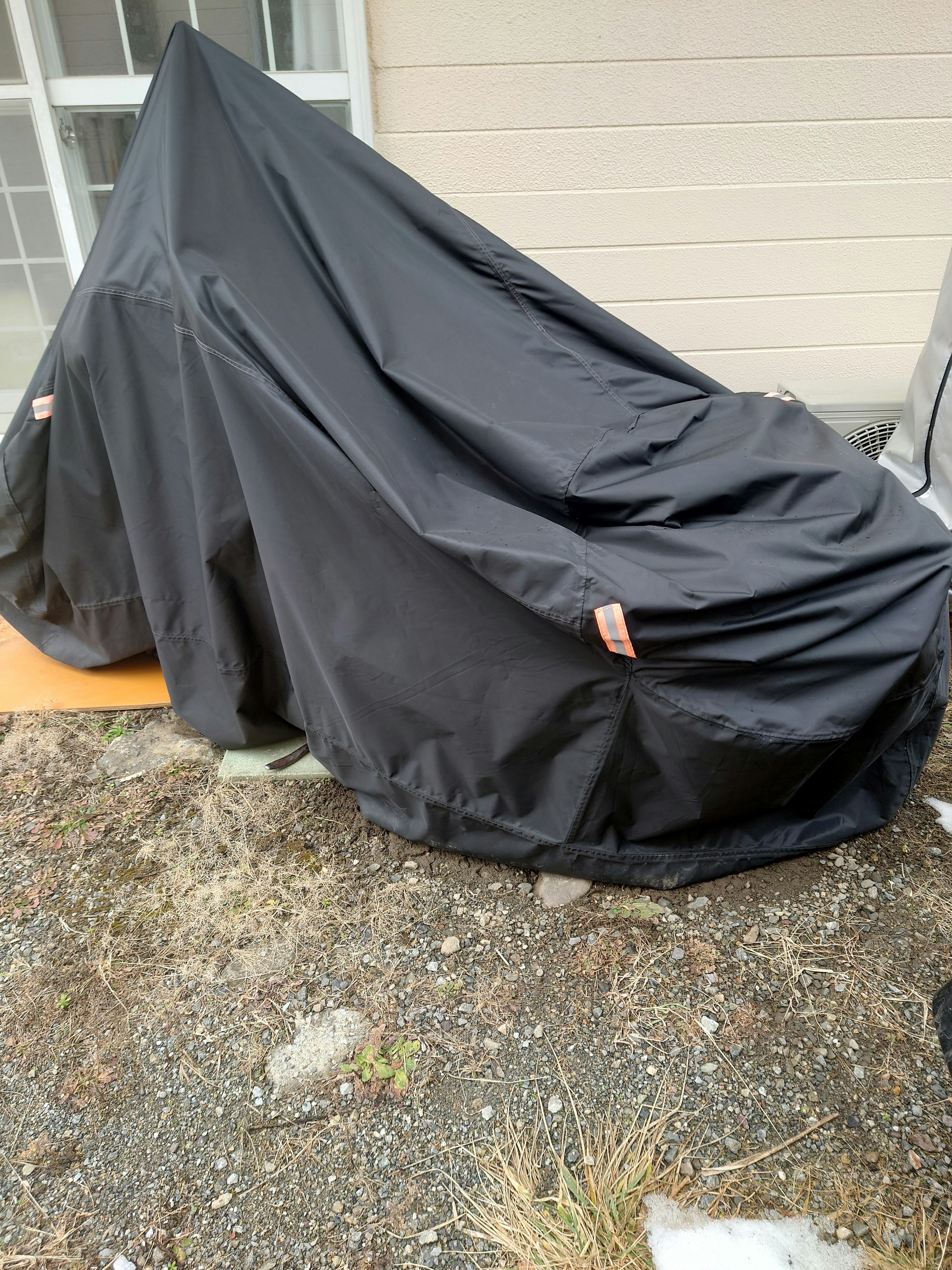 A motorcycle covered with a black tarp is placed outdoors