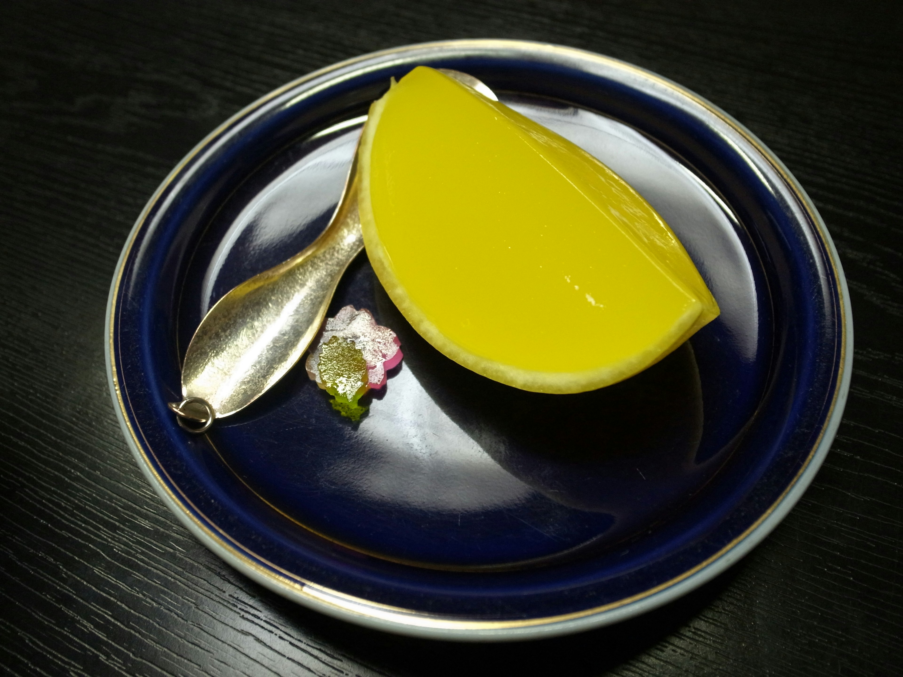 Dessert jaune servi sur une assiette bleue avec une cuillère en argent et une garniture décorative