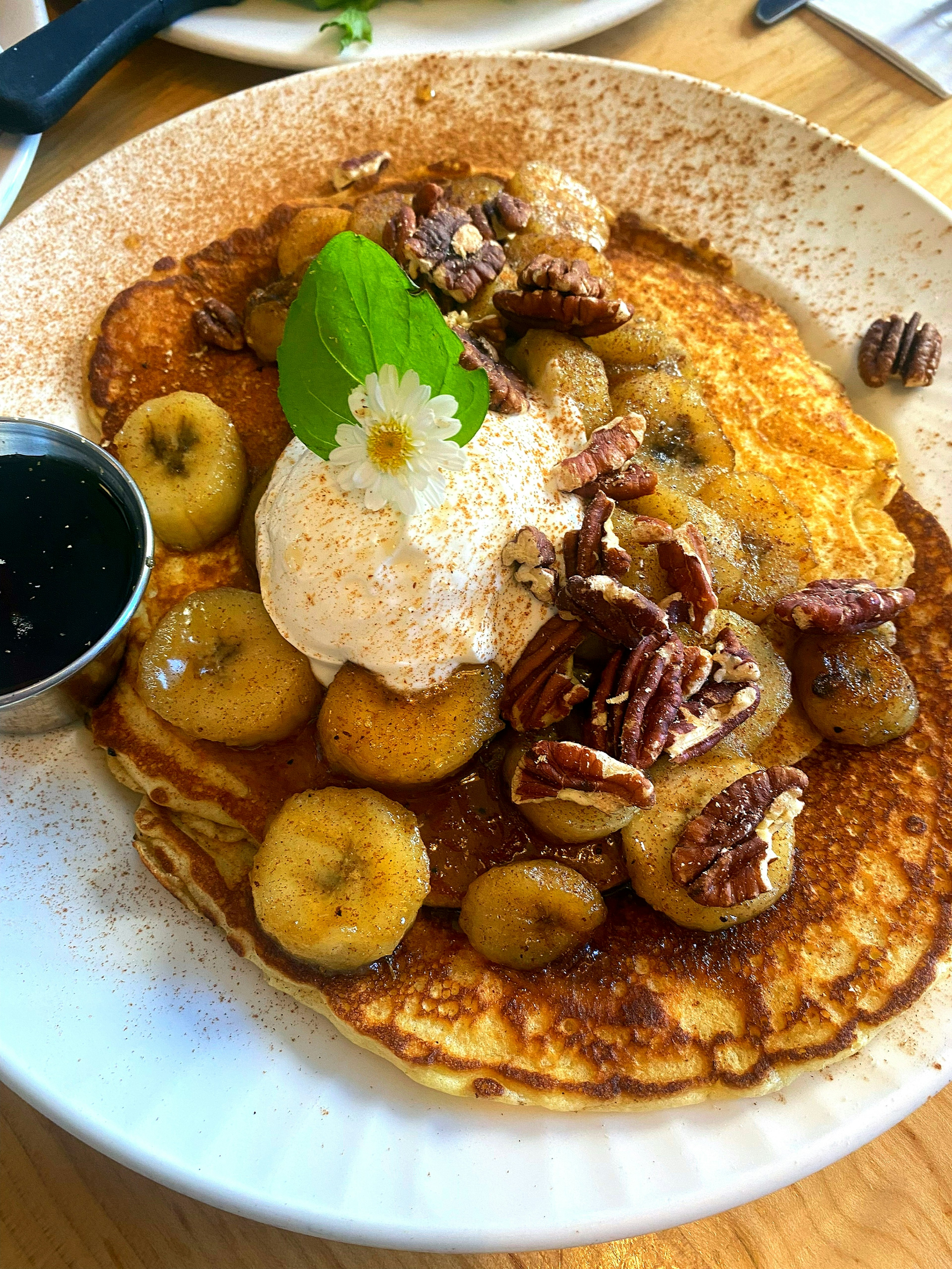 Pancake topped with bananas and pecans served with vanilla ice cream and a mint leaf