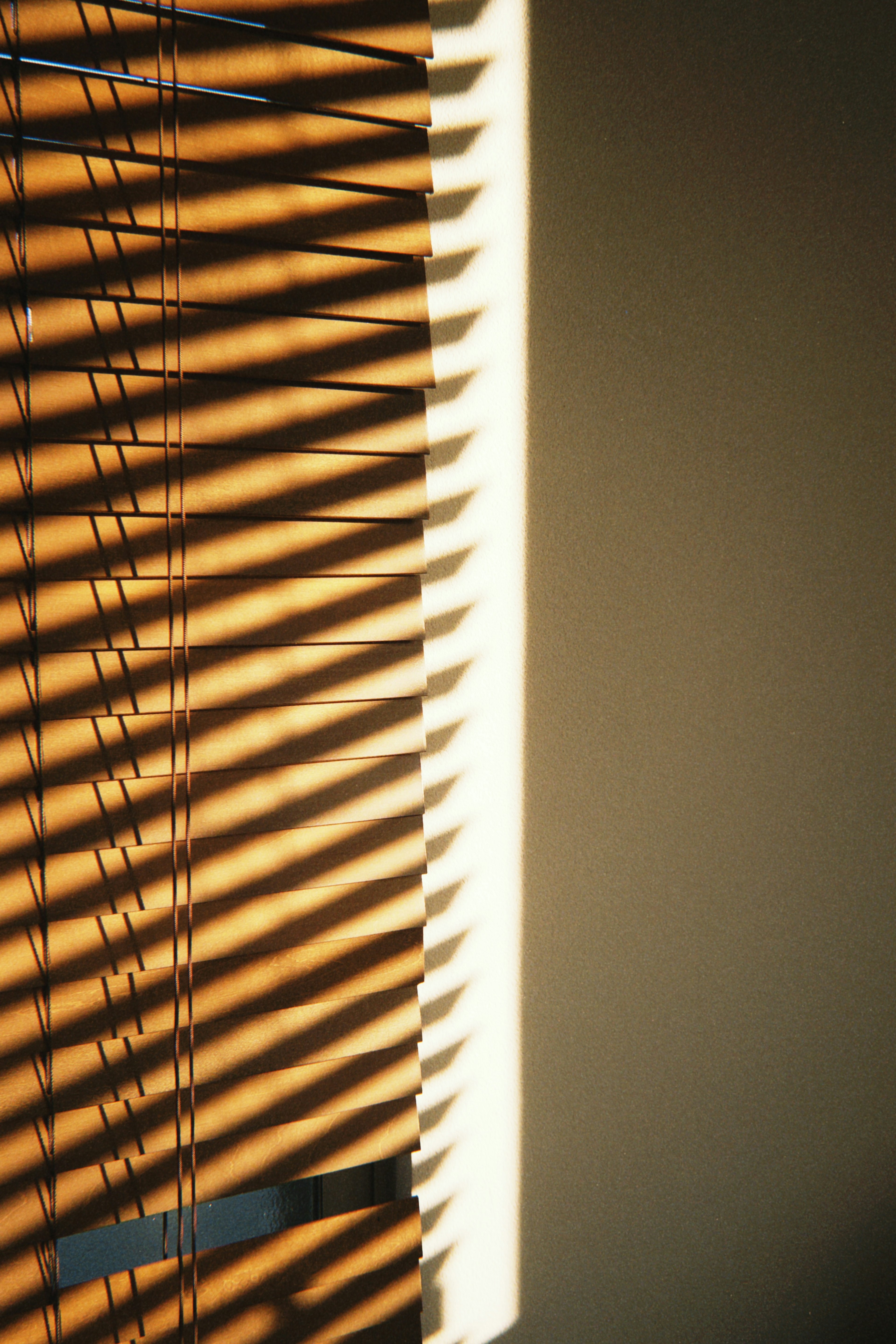 Shadows from wooden blinds cast on a wall in a simple indoor setting