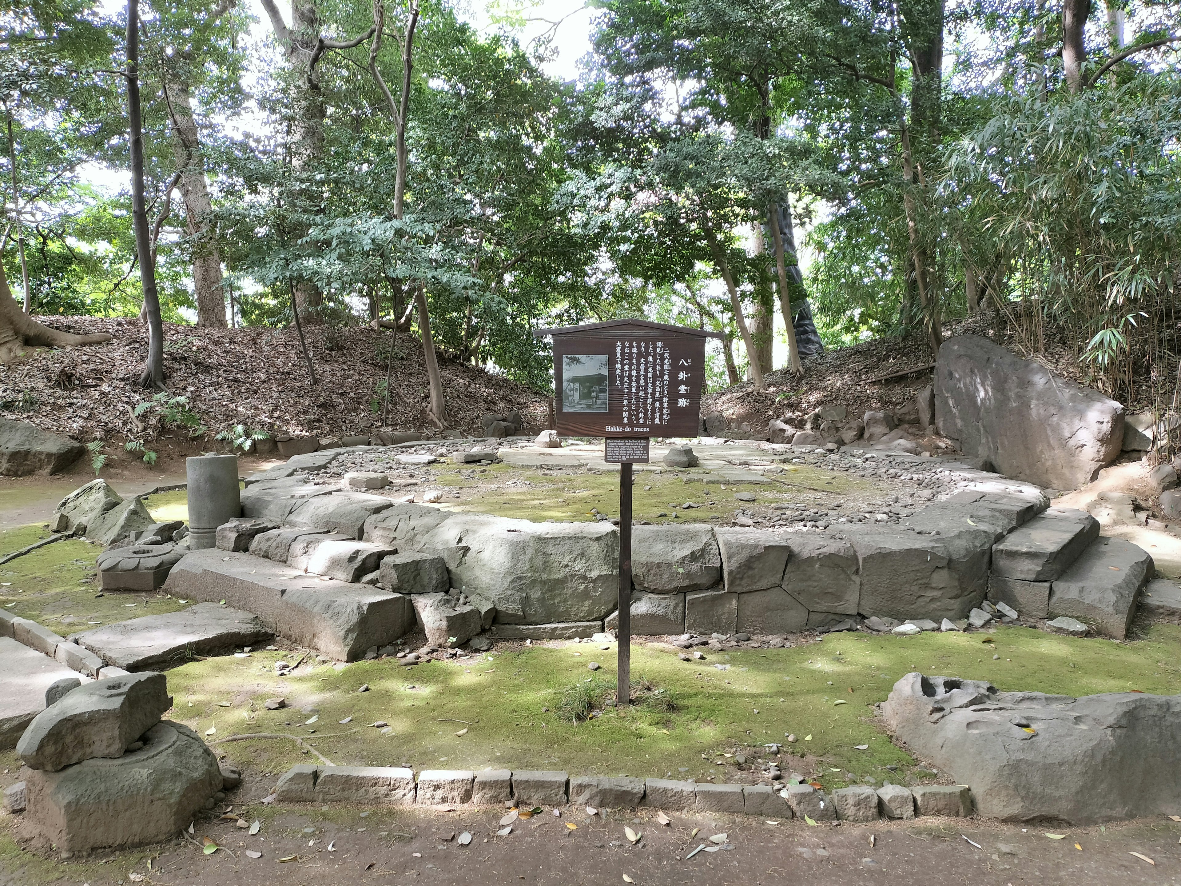 Antiche rovine di pietra circondate da una vegetazione lussureggiante con un cartello informativo