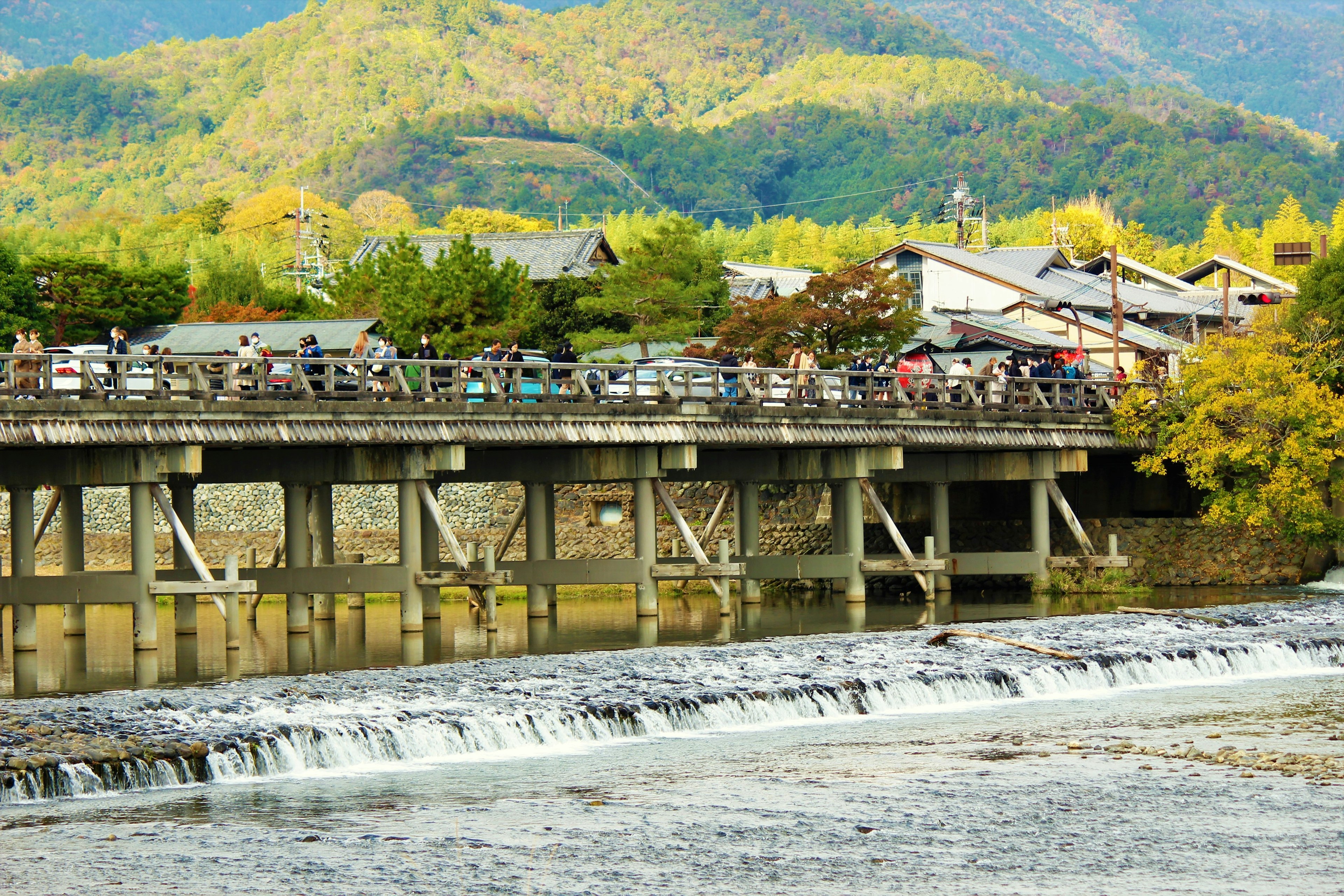 ทิวทัศน์ฤดูใบไม้ร่วงที่มีสะพานข้ามแม่น้ำและภูเขาล้อมรอบ