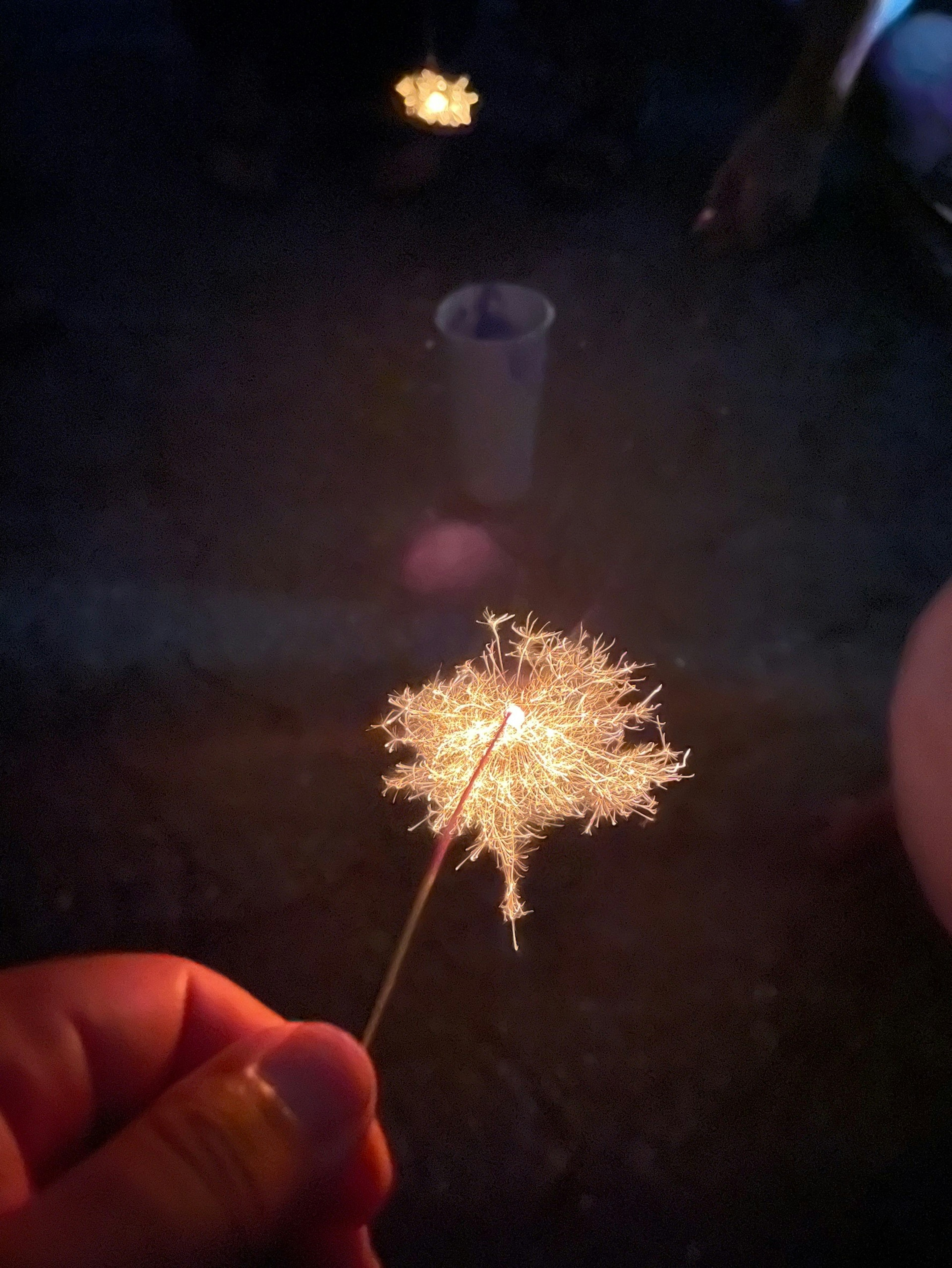 Una mano sosteniendo un fuego artificial chispeante contra un fondo oscuro