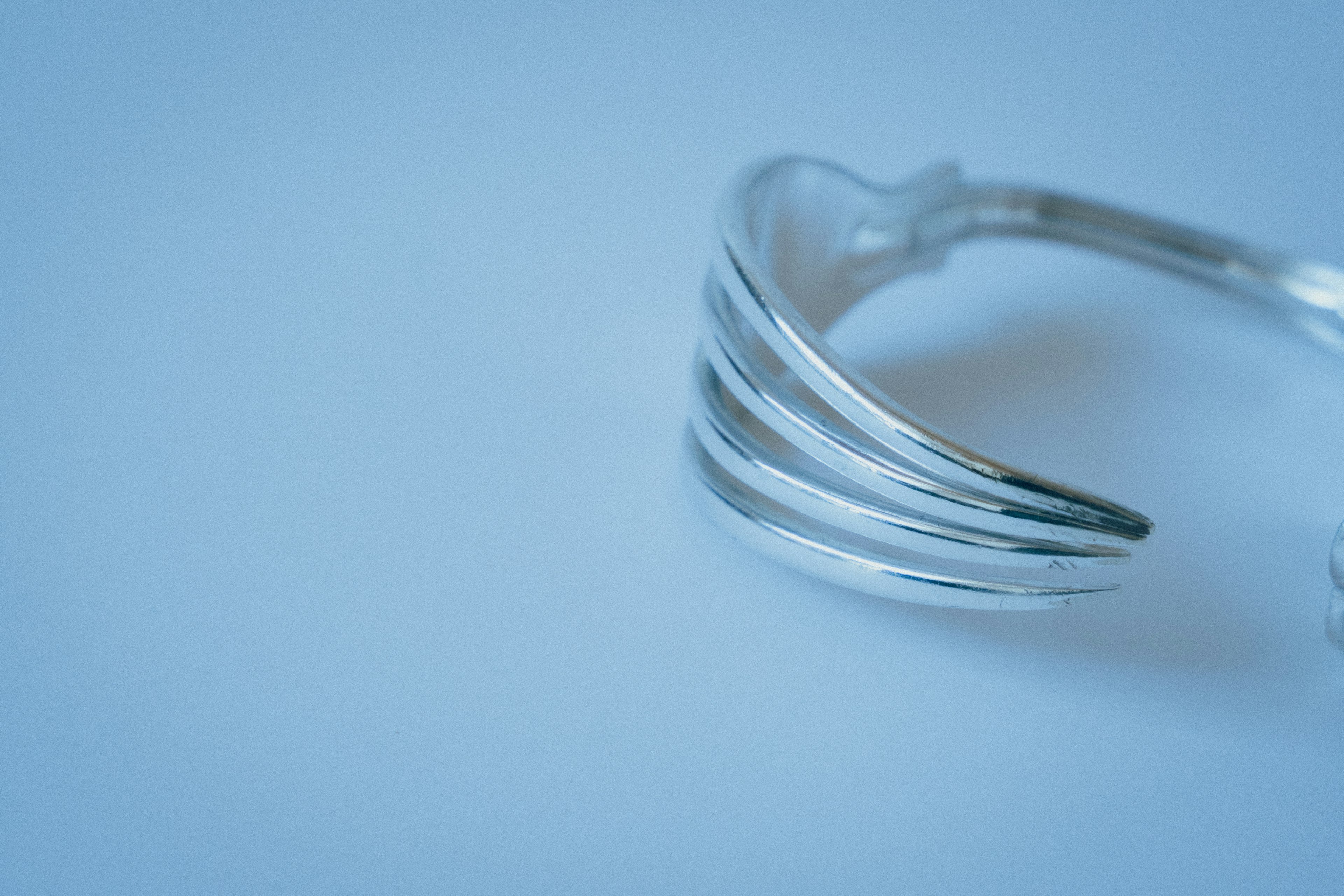 Una pulsera de plata simple y elegante con líneas curvas sobre un fondo azul