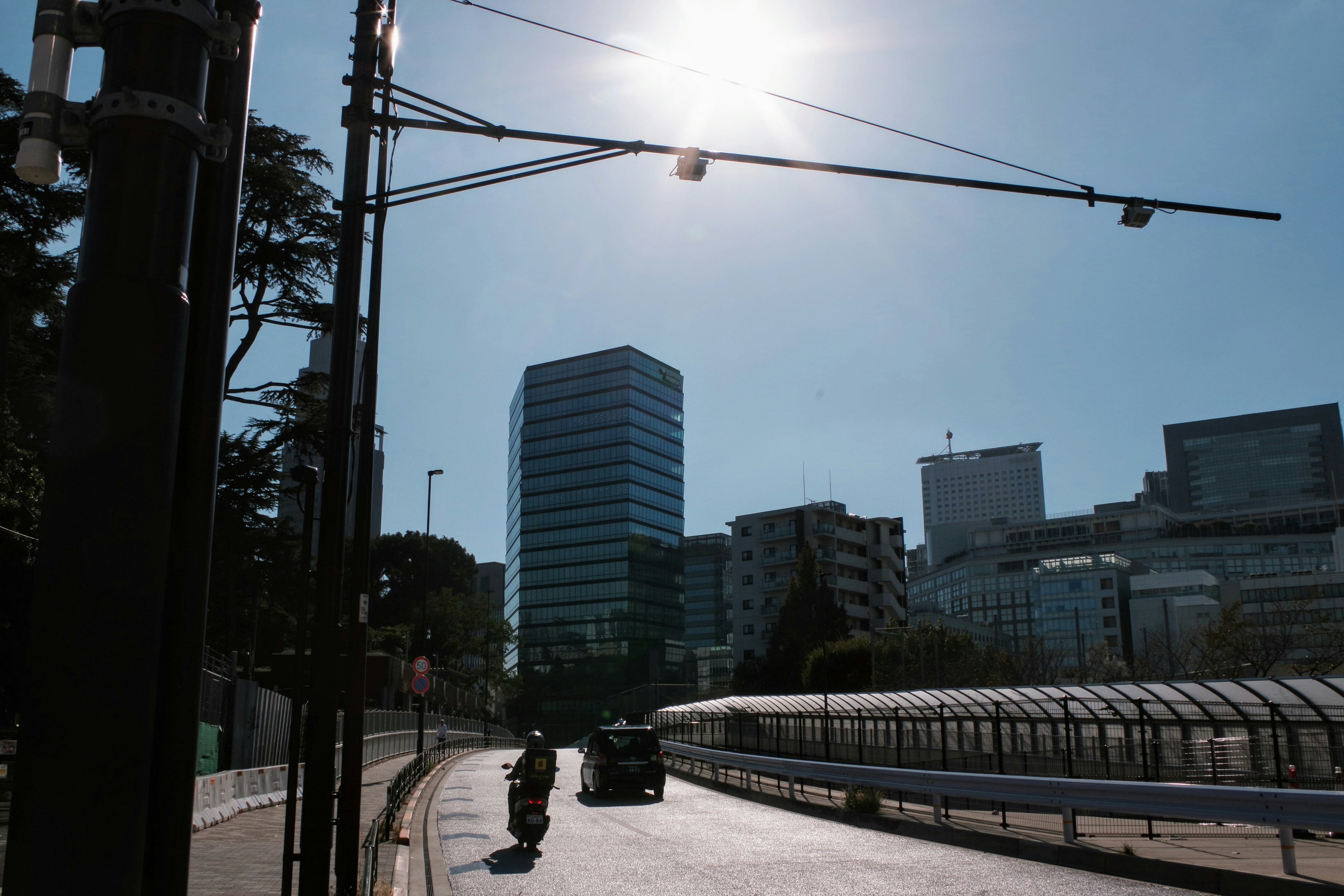 Urban landscape under bright sunlight featuring tall buildings and a road with a motorcycle