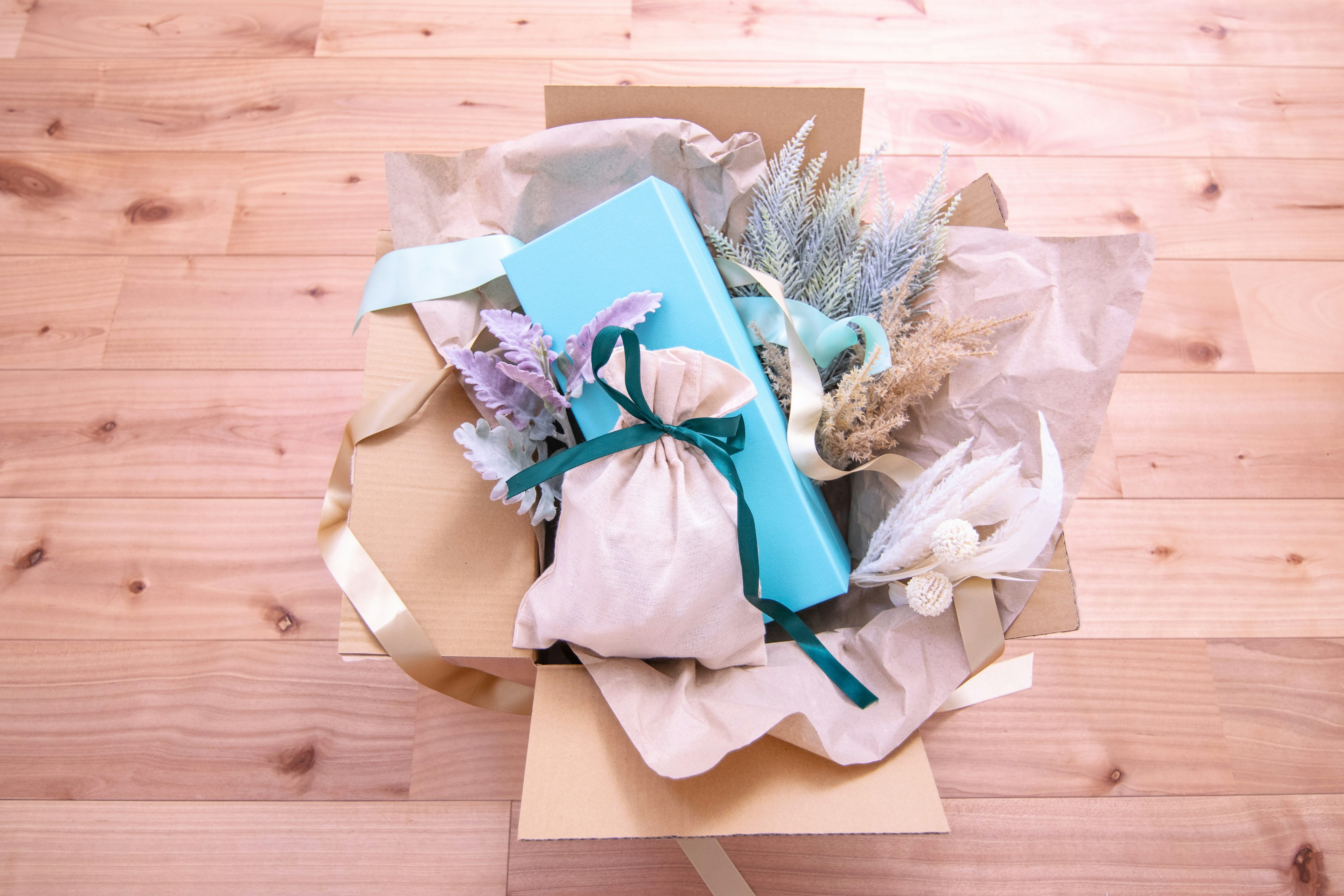 Top view of a gift box filled with a blue gift, dried flowers, and decorative elements