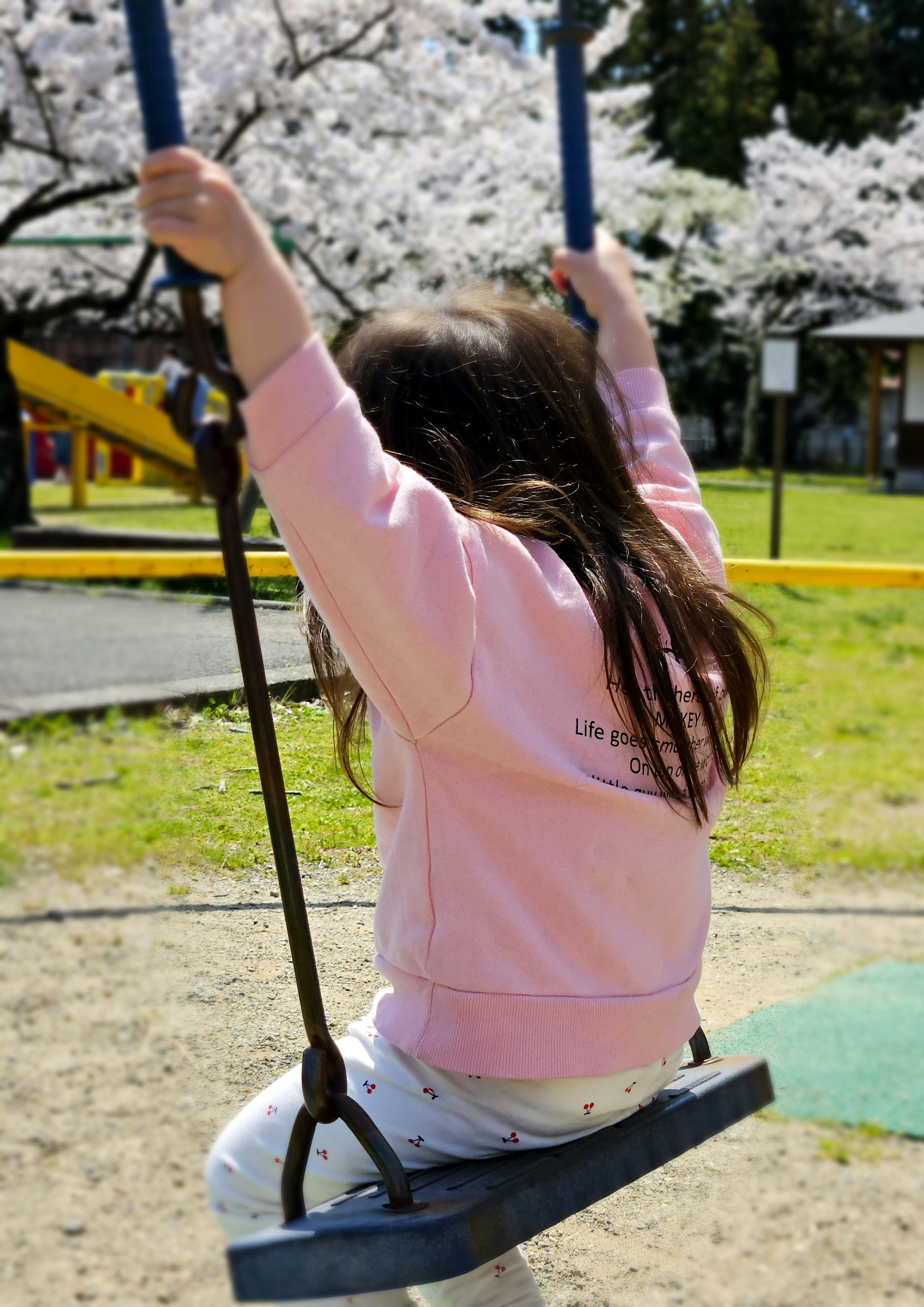 桜の木の下でブランコに乗る子供の後ろ姿