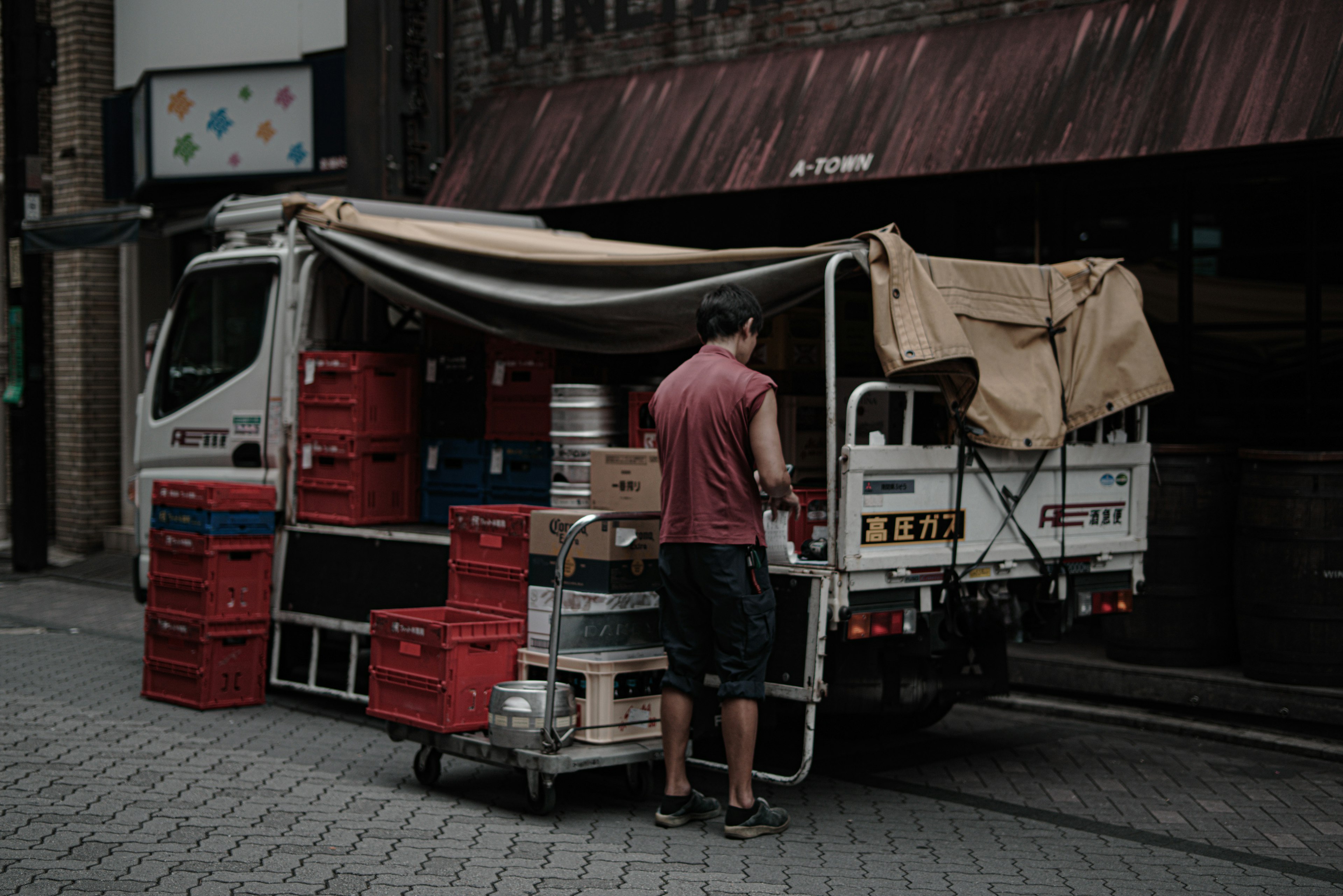 Uomo che lavora sul retro di un camion casse rosse e fusti di birra visibili in strada