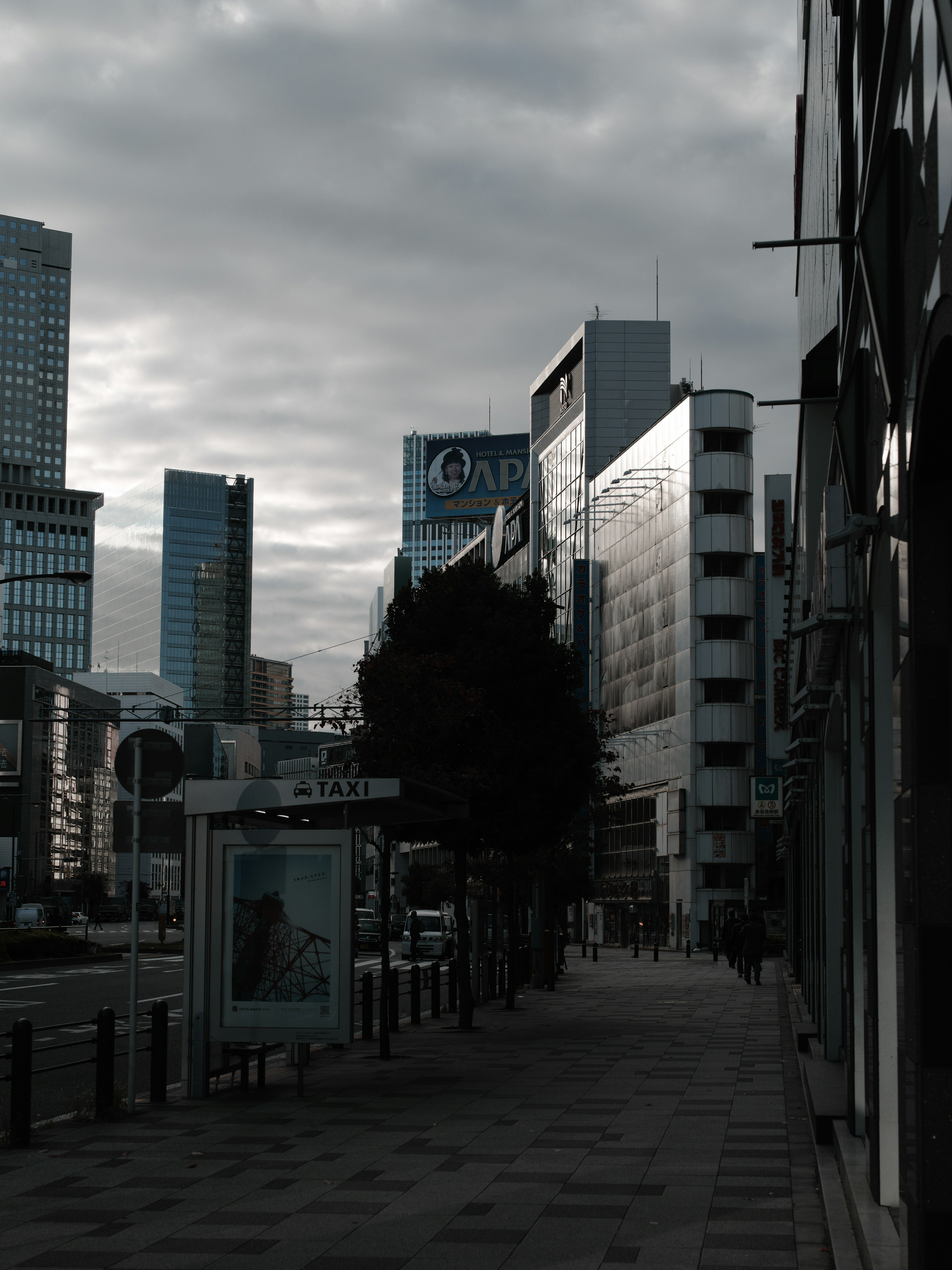 都市の通りの風景で、ビルと木々が並んでいる曇りの日の画像