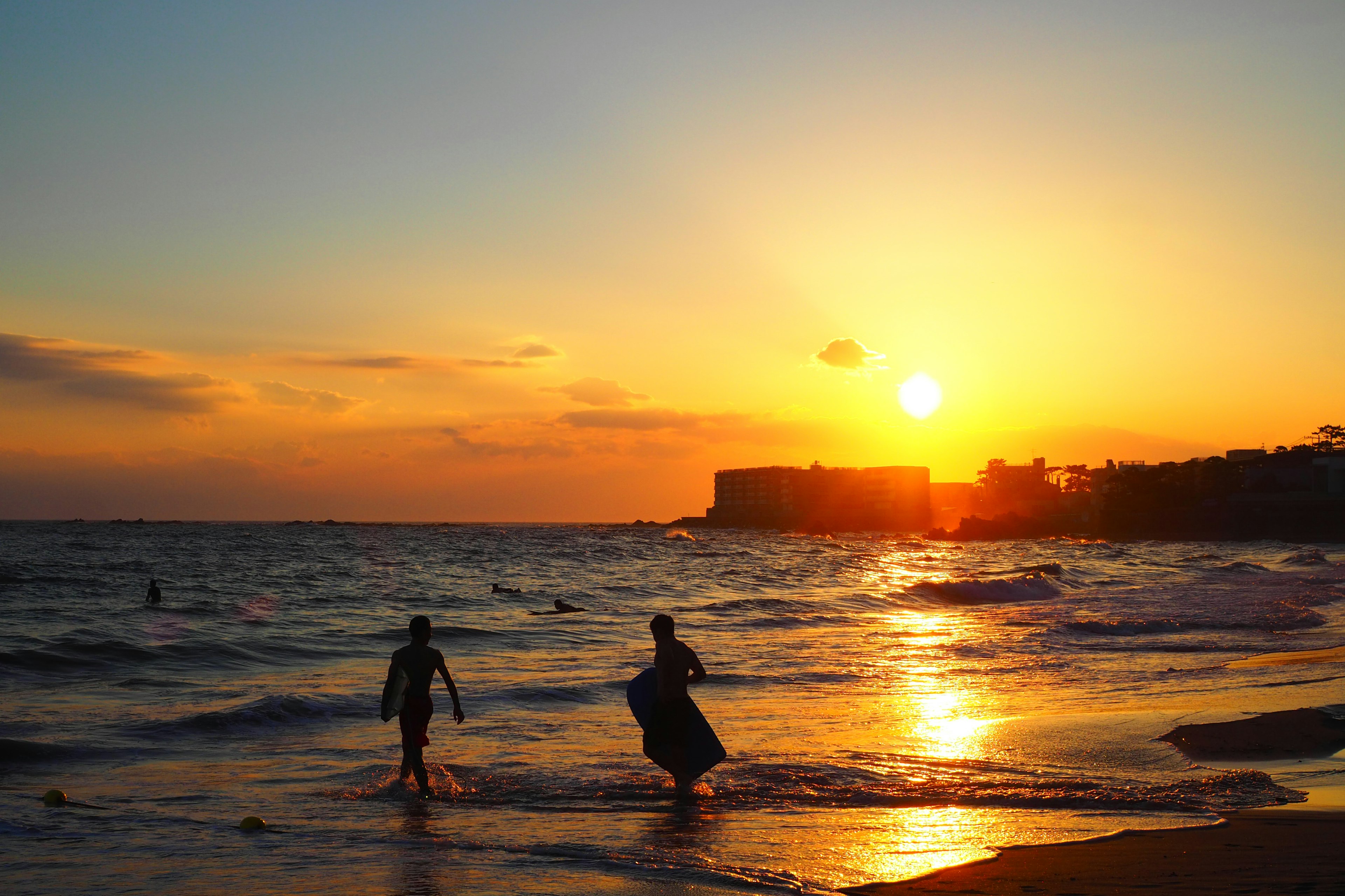 Silhouetten von zwei Personen, die am Meer spielen mit einem Sonnenuntergang im Hintergrund