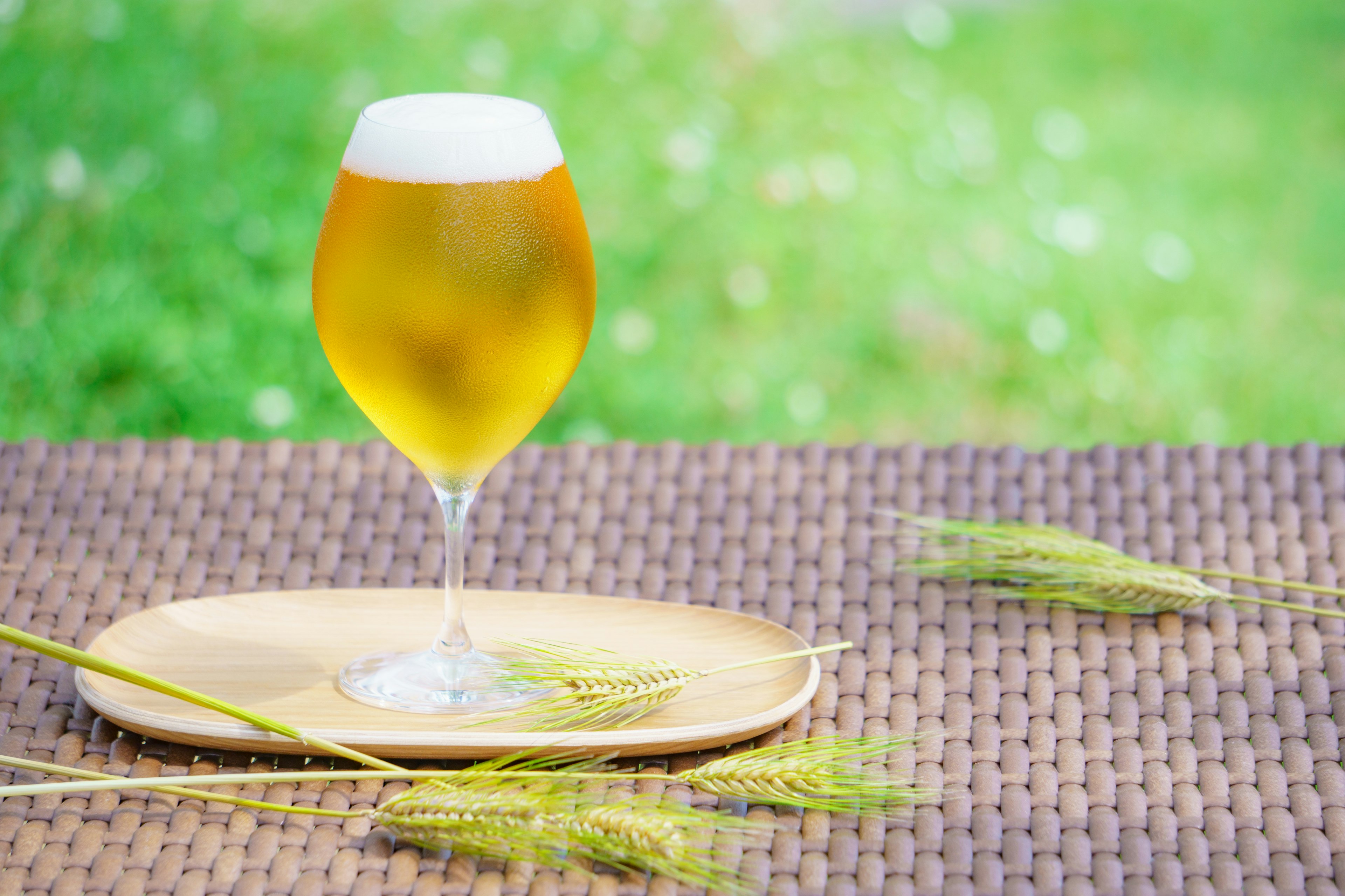 A glass of beer on a wooden plate with wheat stalks outdoors