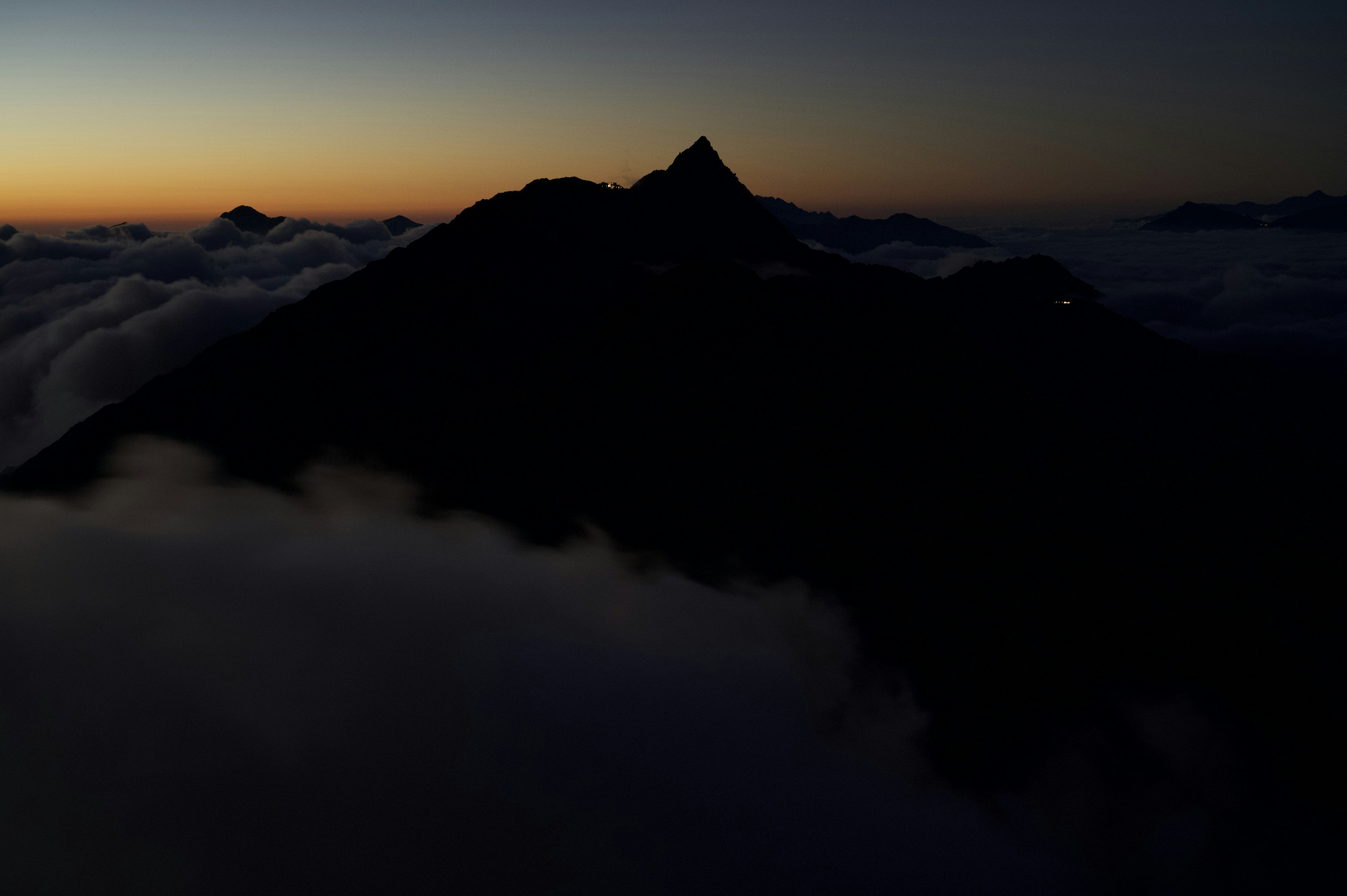 Silhouette of a mountain at dusk surrounded by clouds