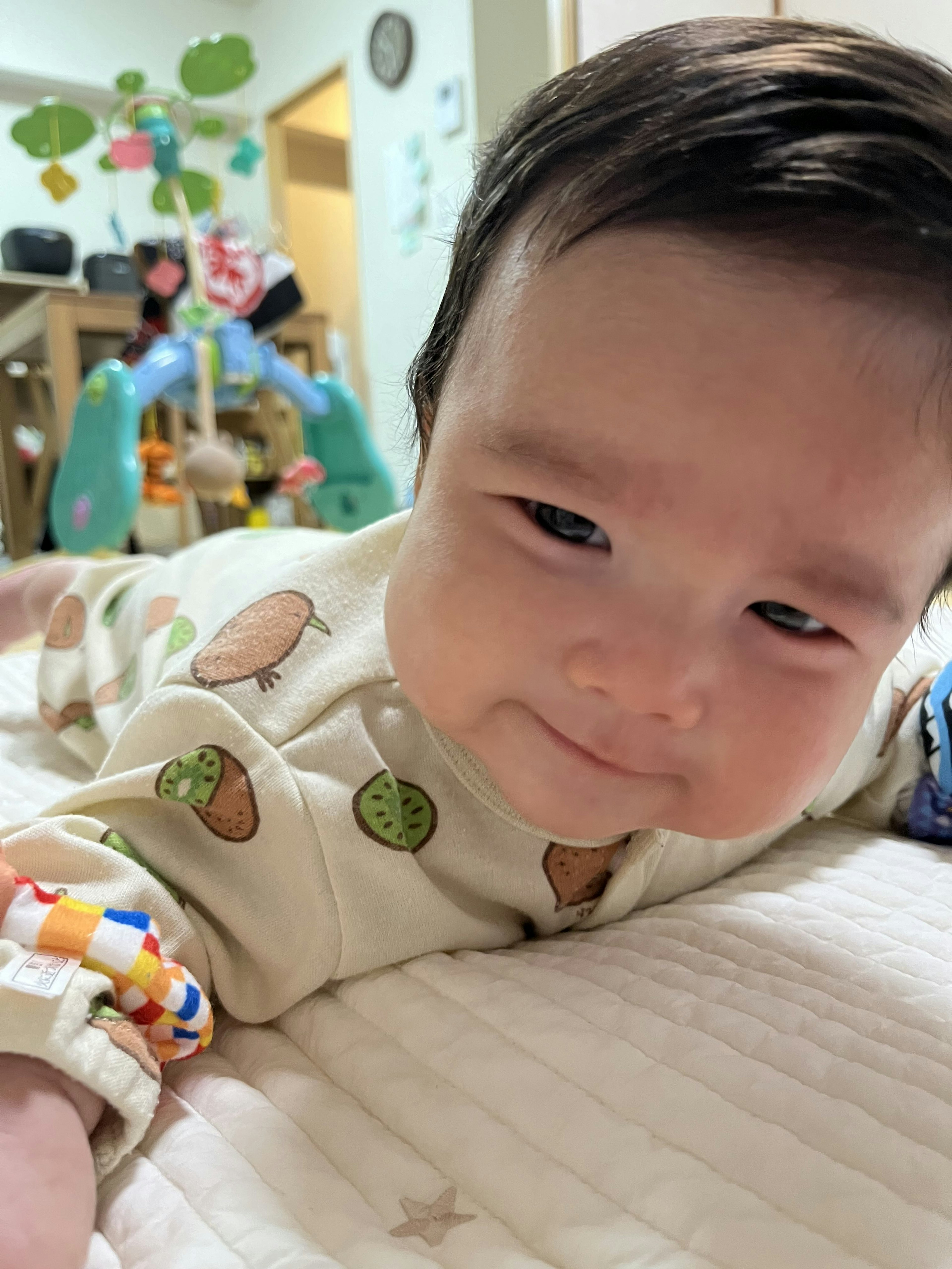 An infant lying on a bed smiling with toys and cute patterned clothing in the background