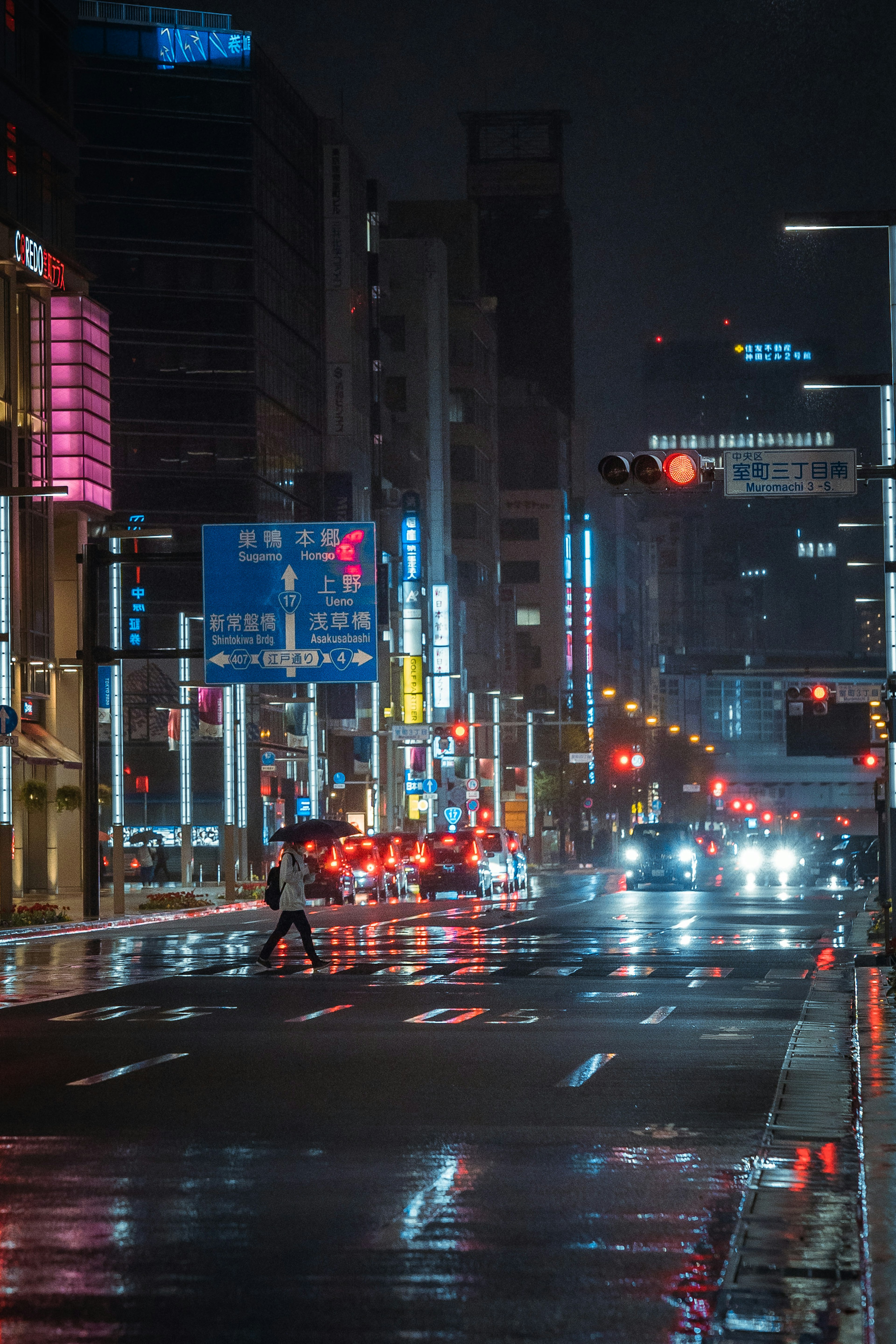 夜の街並みで雨に濡れた道路を渡る人影とネオンの看板