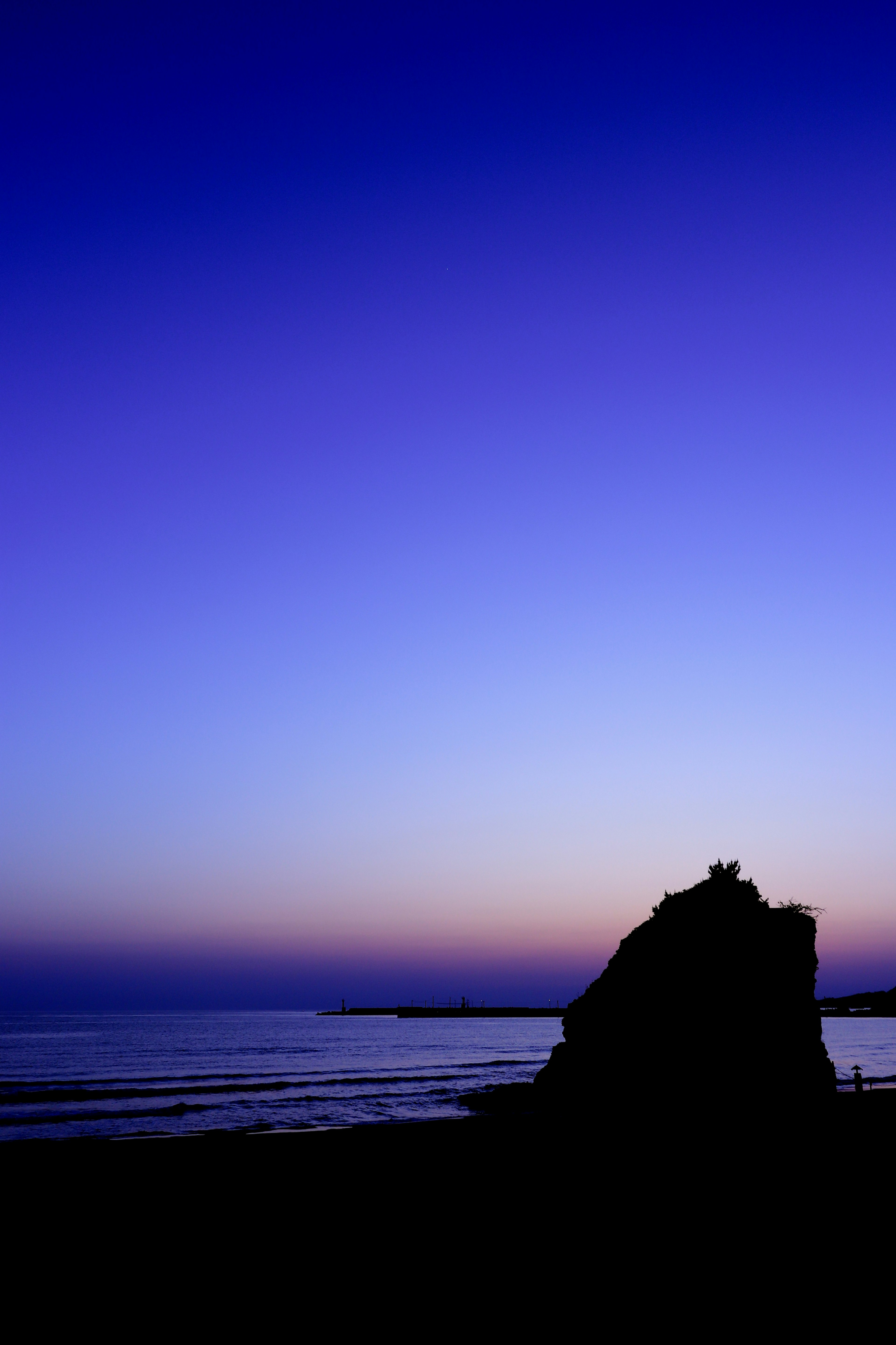 Beautiful sunset landscape featuring silhouettes of the sea and a rock