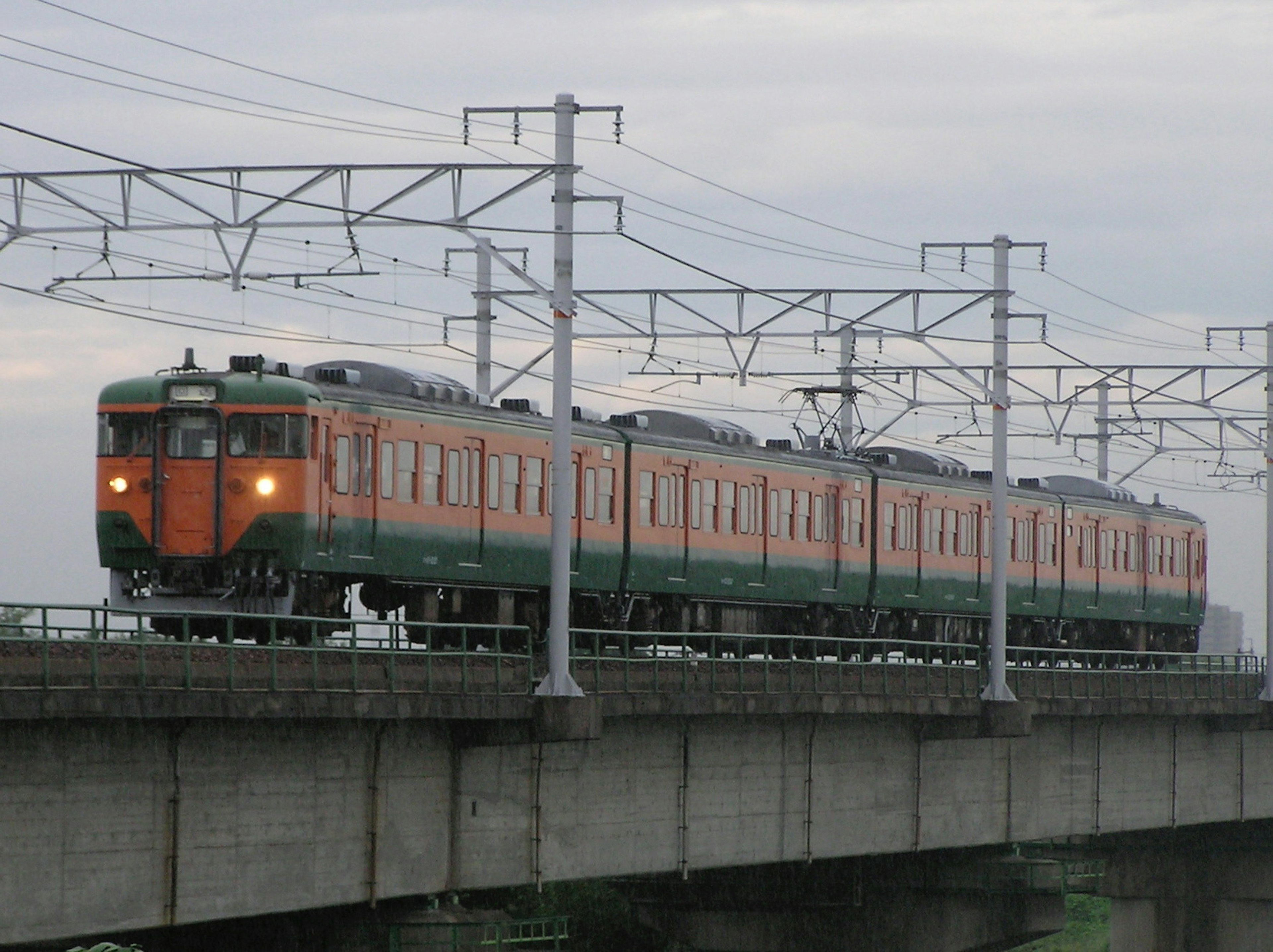 Treno arancione e verde che corre su un binario elevato