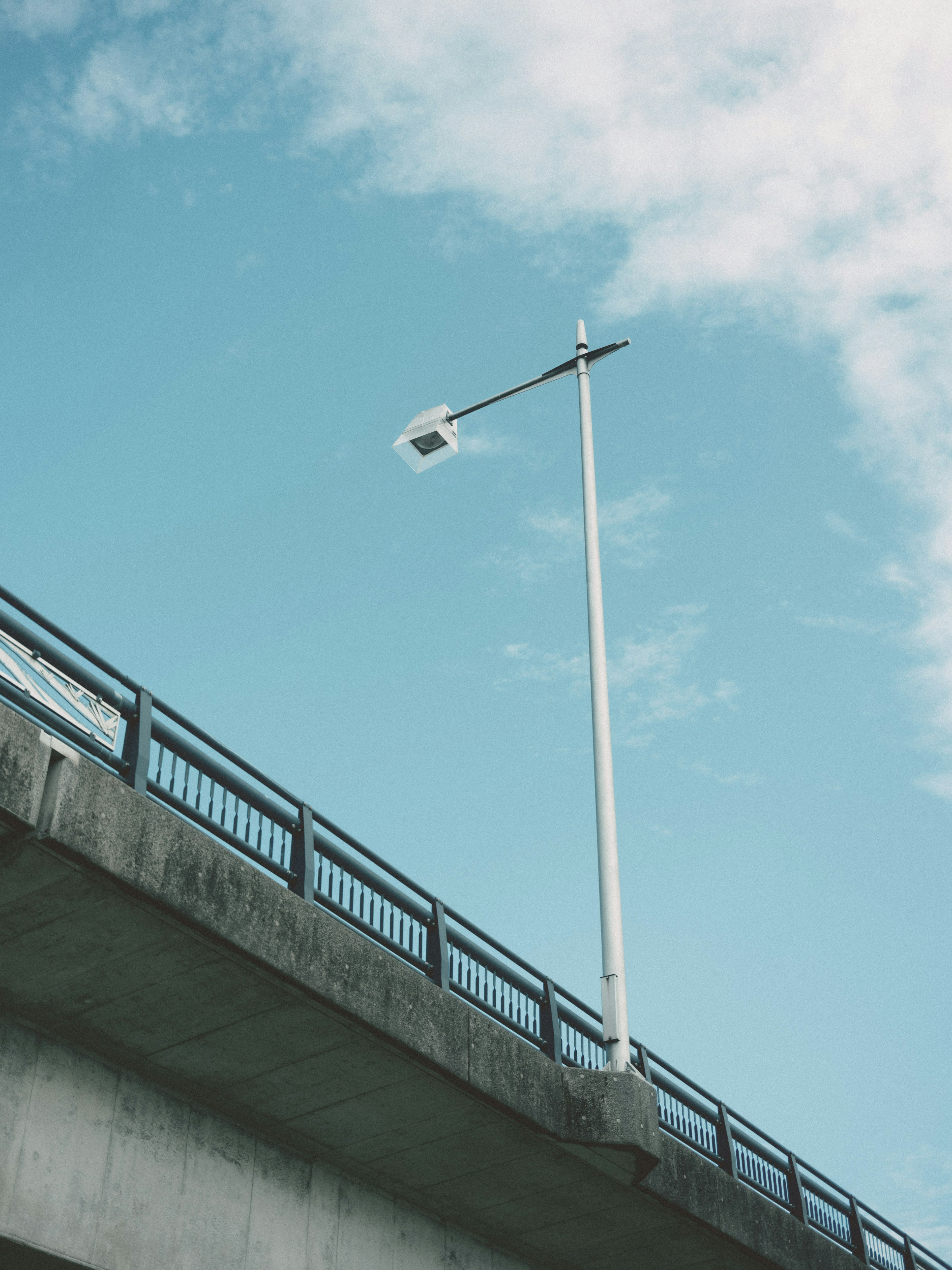 A white streetlight under a blue sky on a bridge