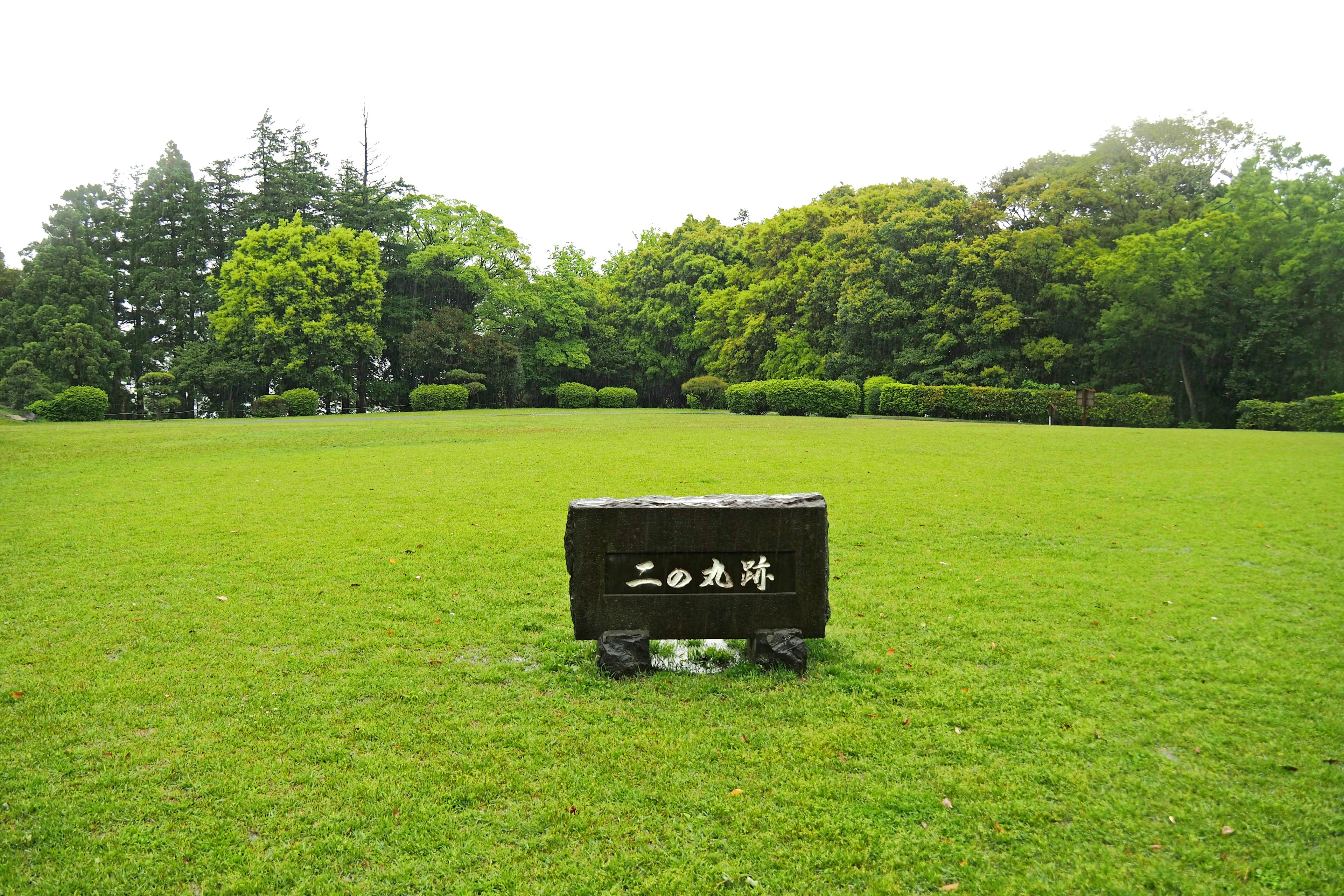 Ein Steinschild in einem weitläufigen grünen Park mit Bäumen im Hintergrund