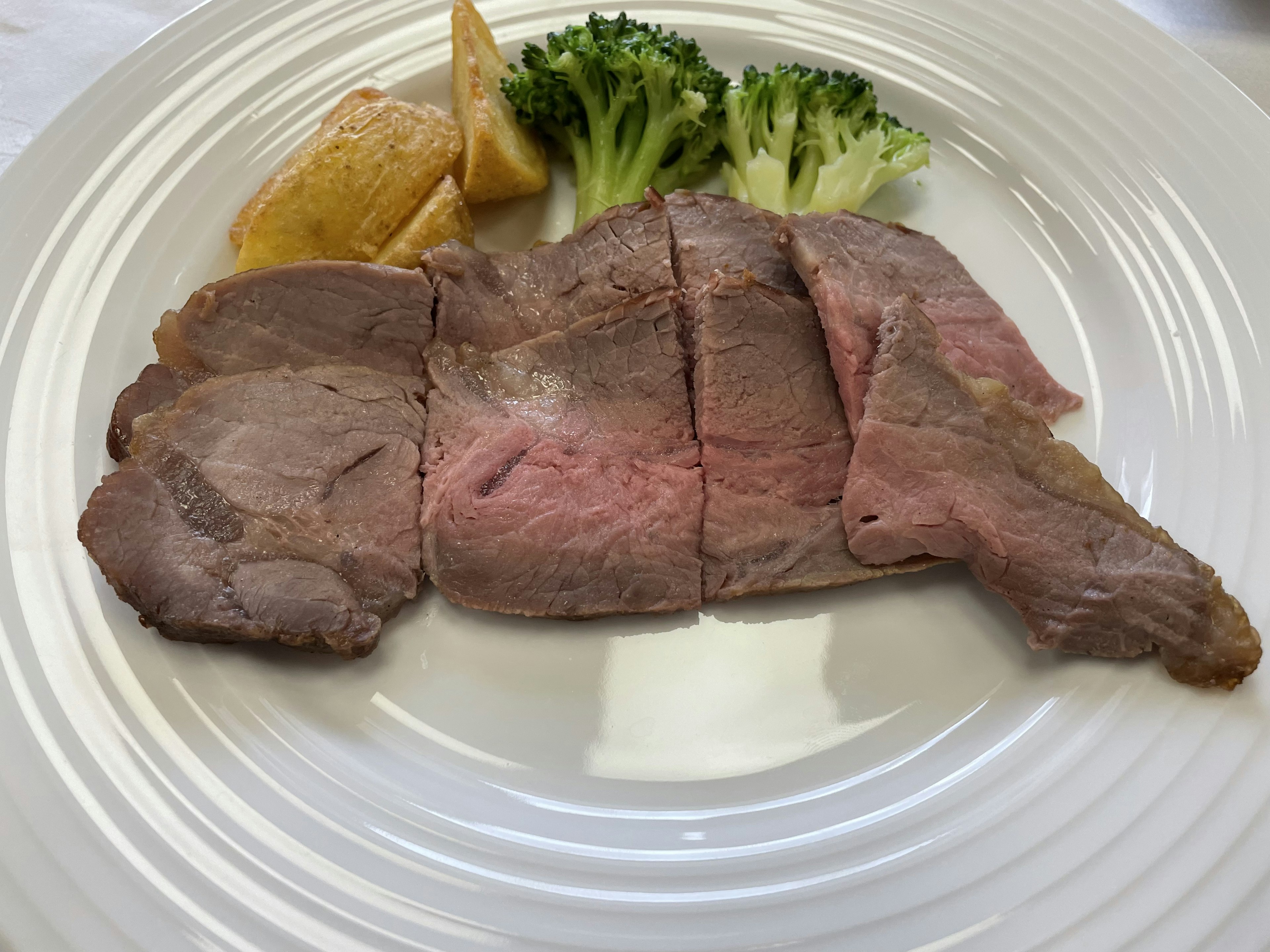 Sliced roast beef on a plate with broccoli and potato wedges