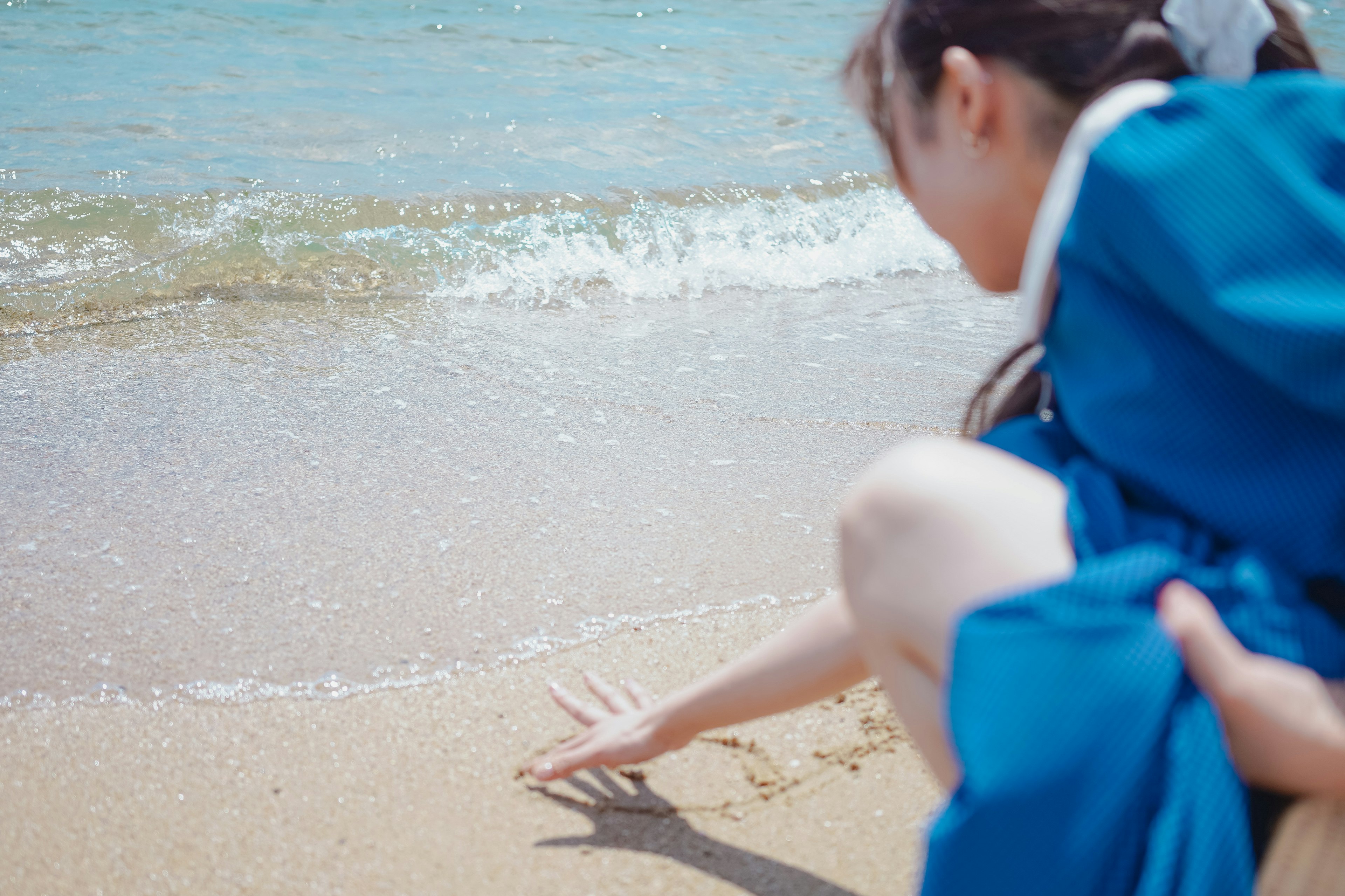 穿著藍色裙子的女孩在海灘上觸摸沙子