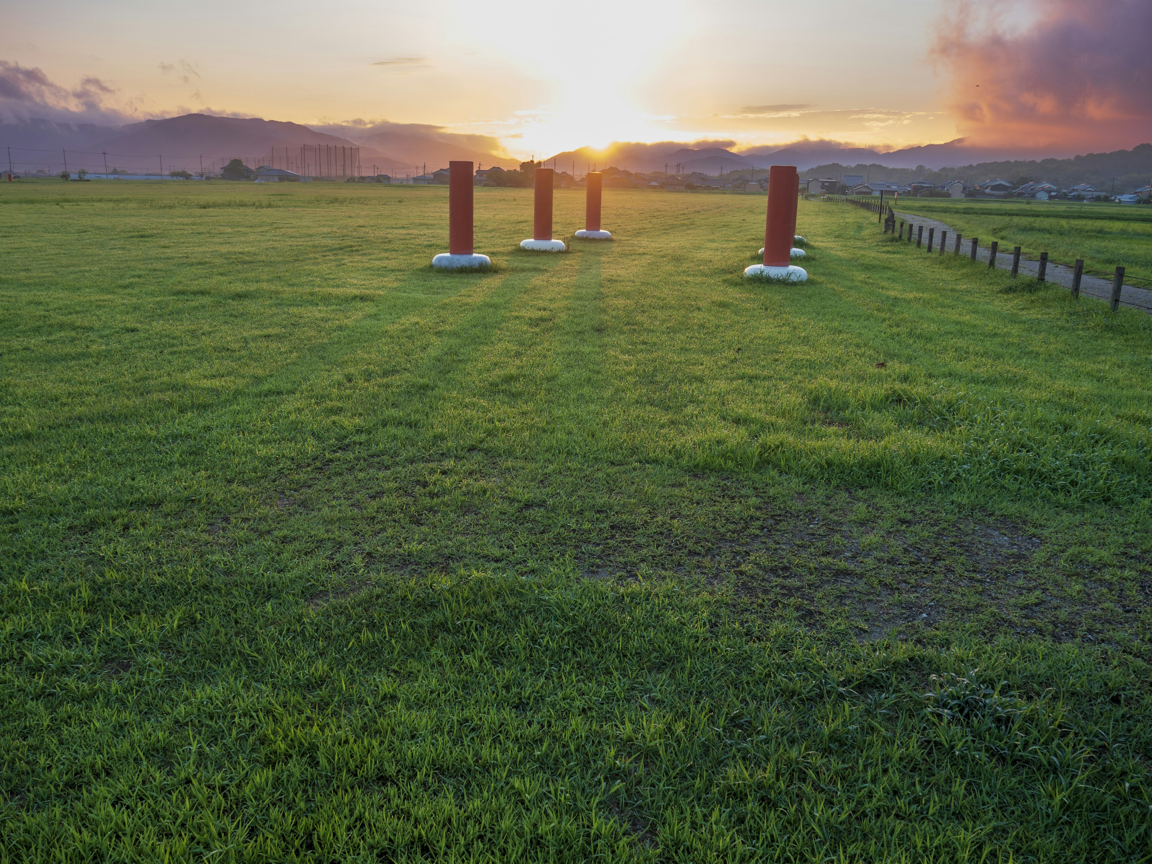 Pilares rojos en un campo de hierba al atardecer con montañas al fondo