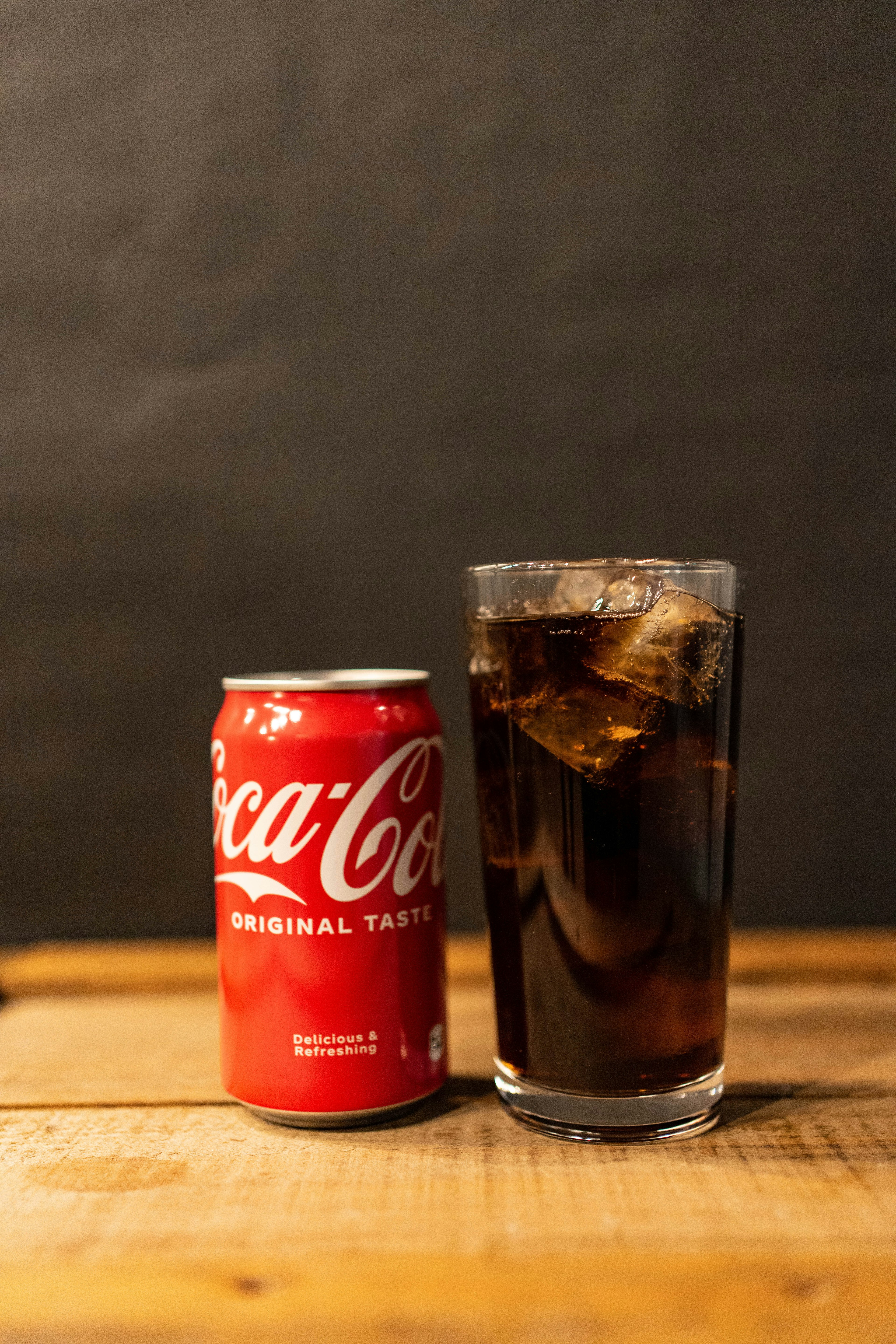 Lata de Coca-Cola junto a un vaso lleno de hielo y cola sobre una mesa de madera