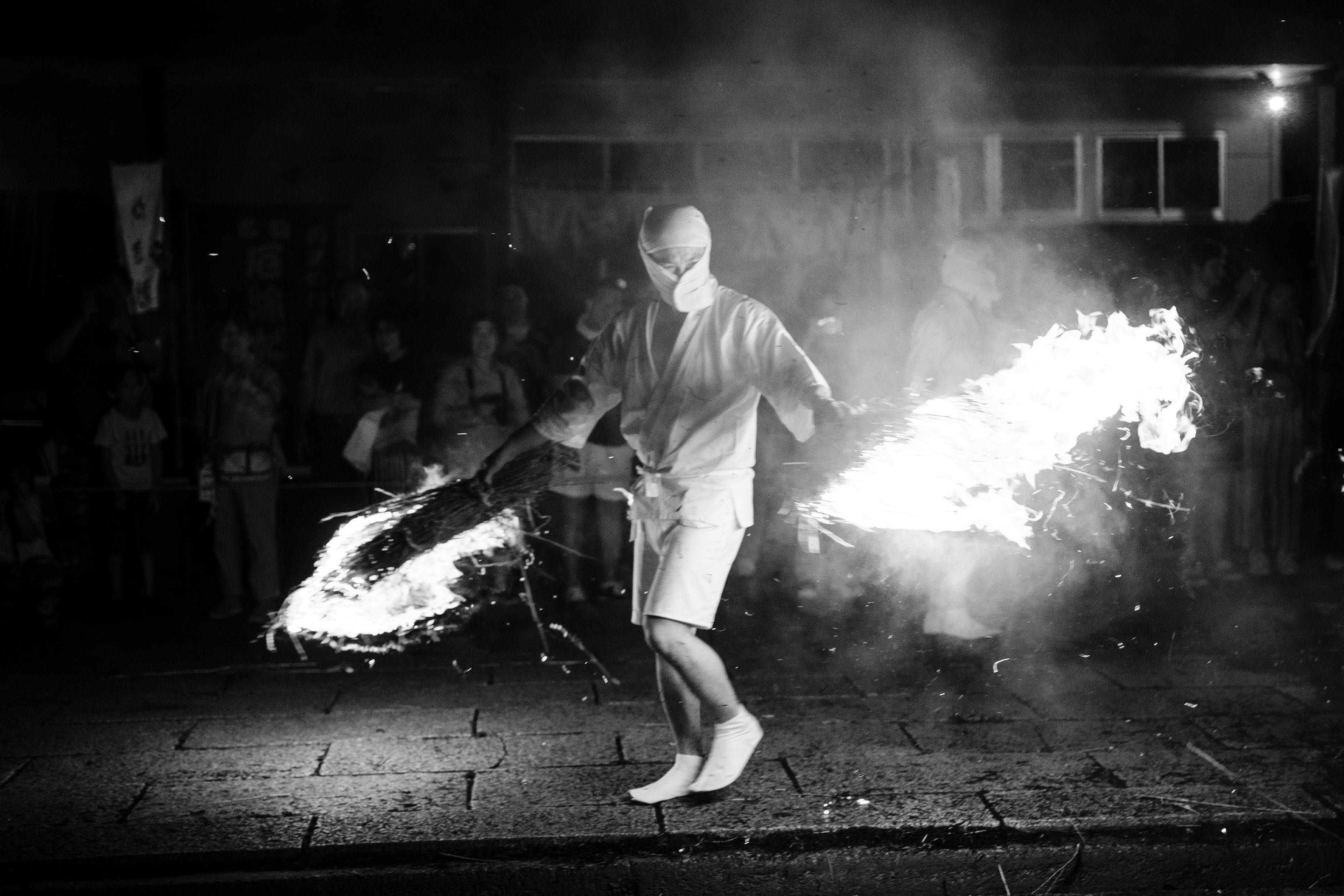 Image en noir et blanc d'un artiste dansant avec du feu devant un public