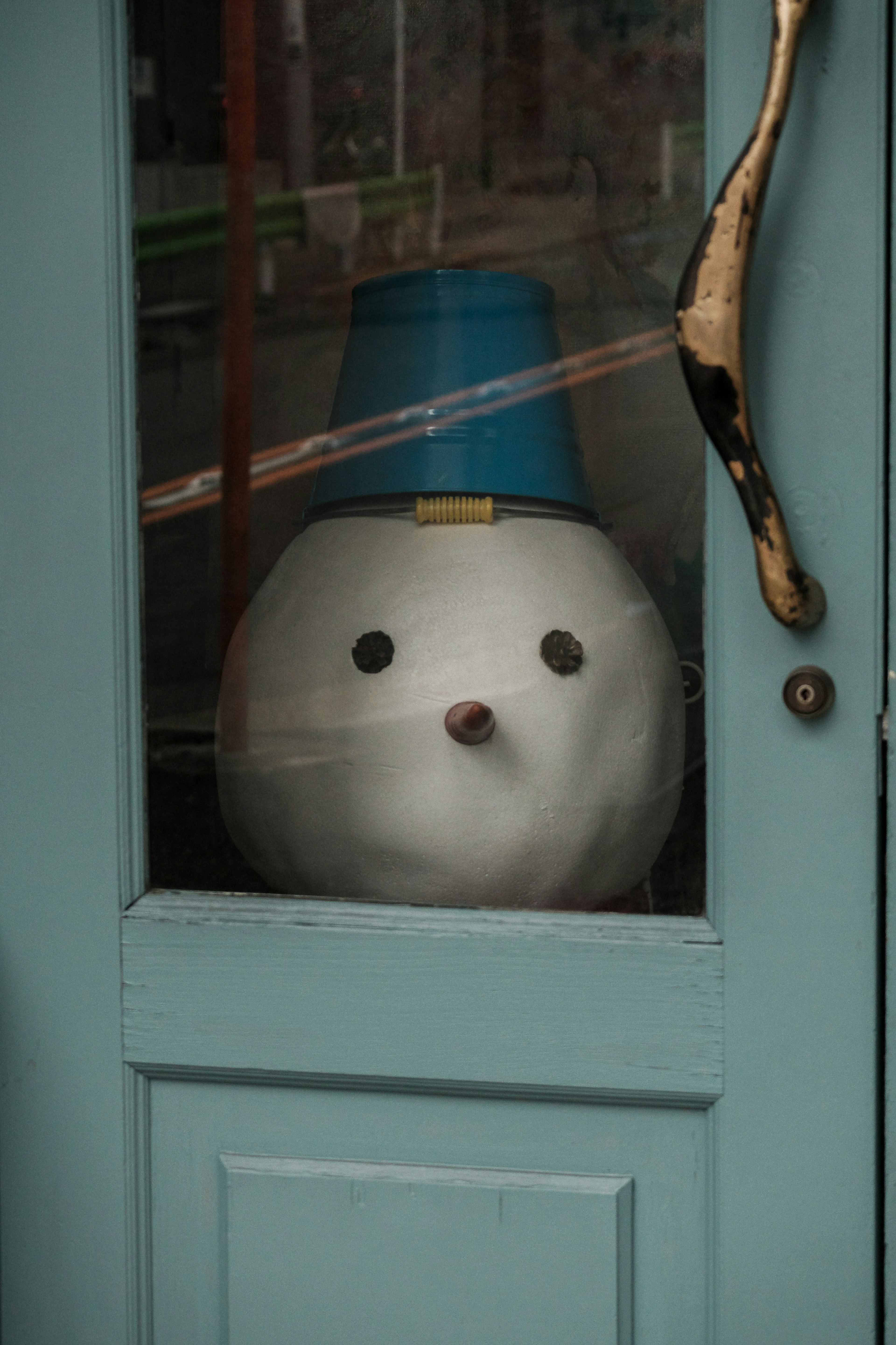 Ein Schneemannkopf mit einem blauen Hut, sichtbar durch eine Glastür