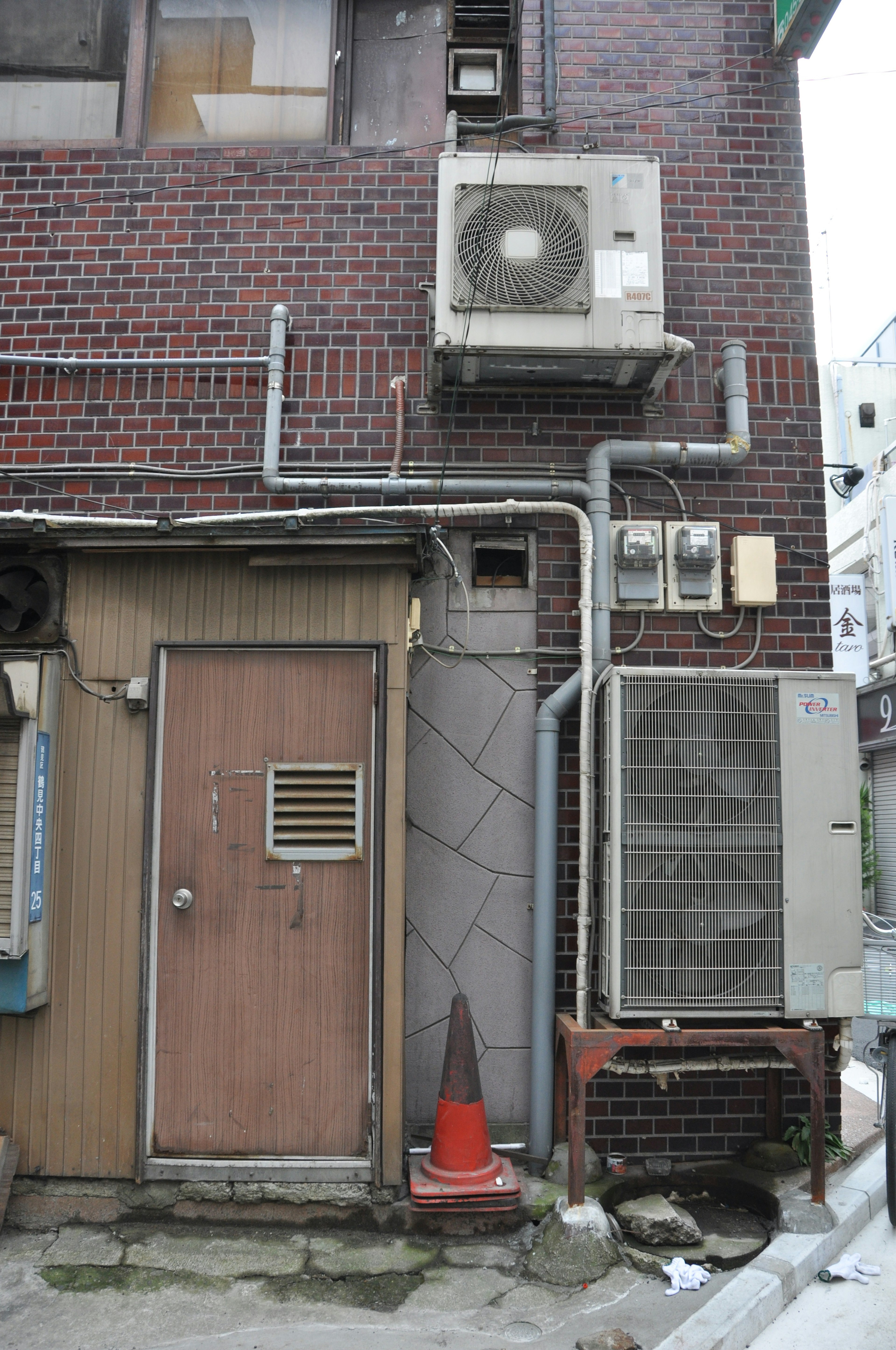 Back entrance of a building with a brick wall featuring air conditioning units and visible piping