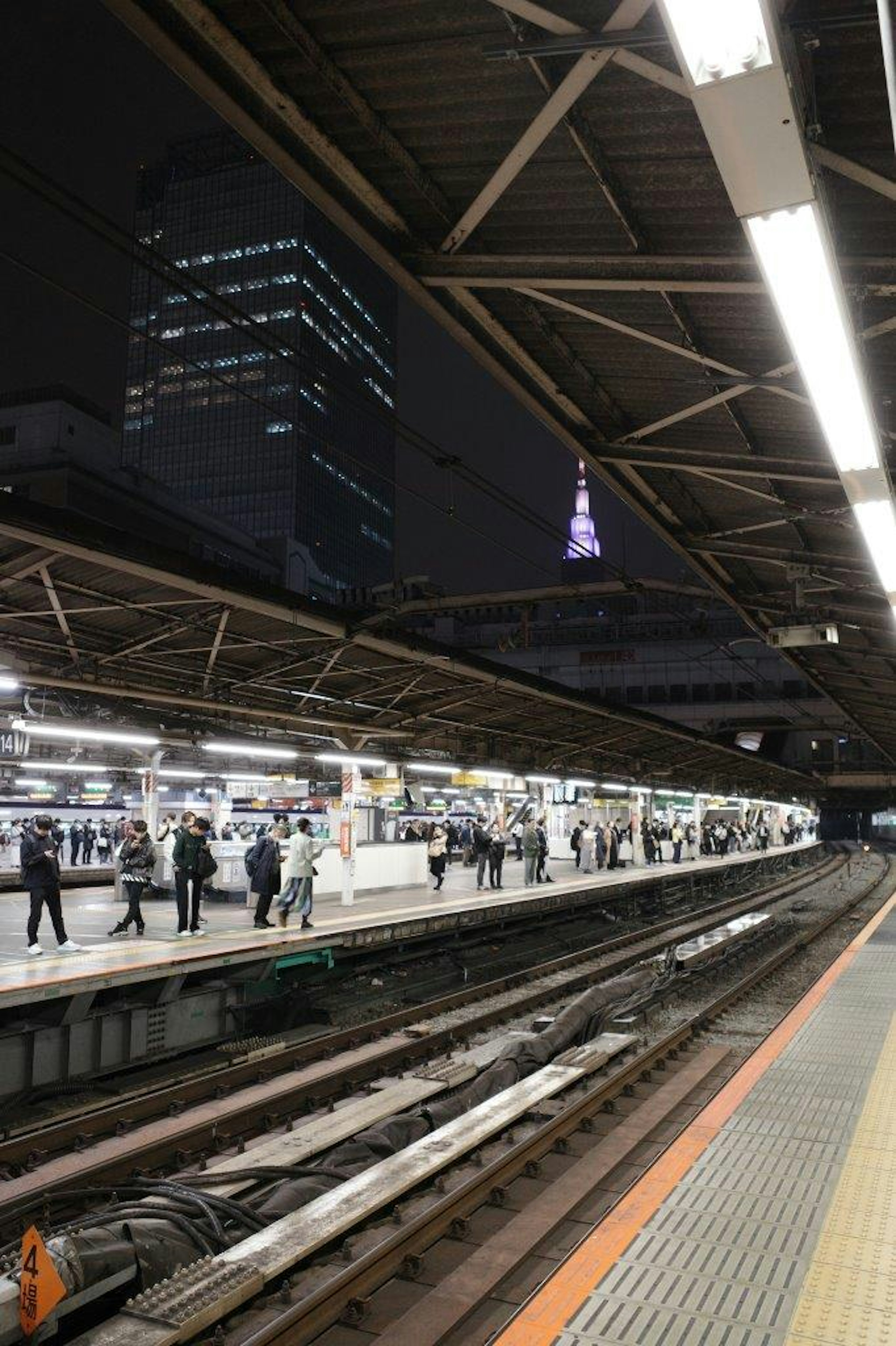 Piattaforma della stazione notturna con persone e grattacieli sullo sfondo che mostrano la Tokyo Tower