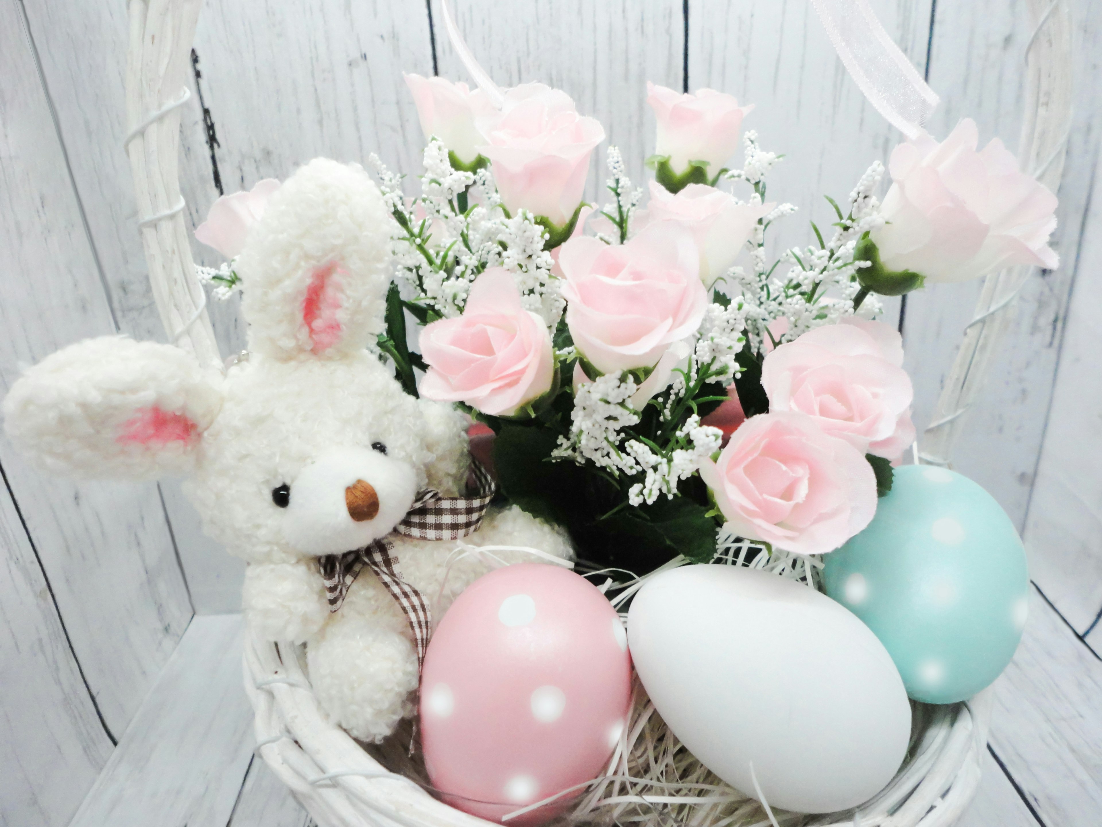 Un adorable jouet en peluche de lapin aux côtés de roses roses dans un panier avec des œufs de Pâques colorés