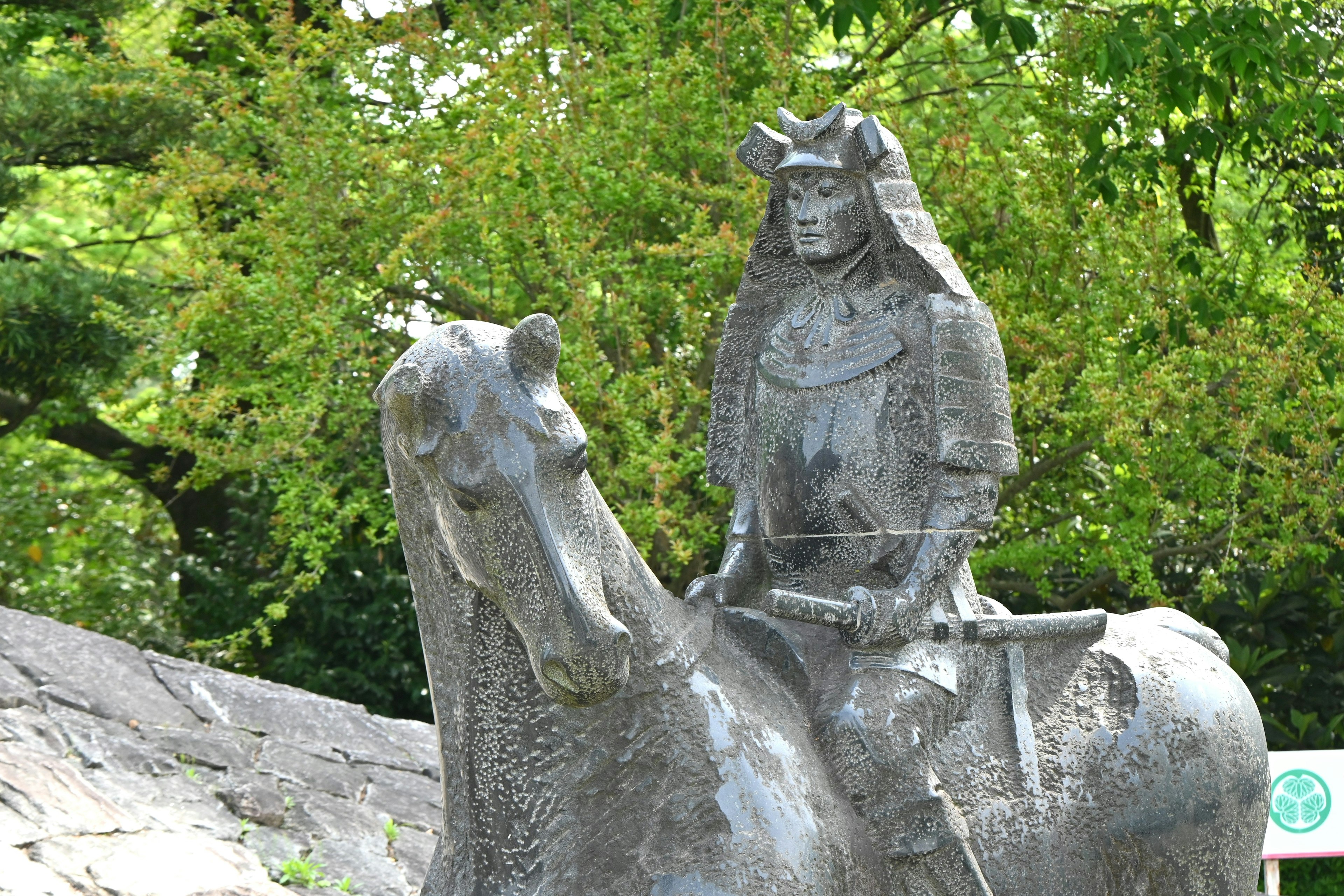 Estatua de bronce de un samurái a caballo rodeada de vegetación