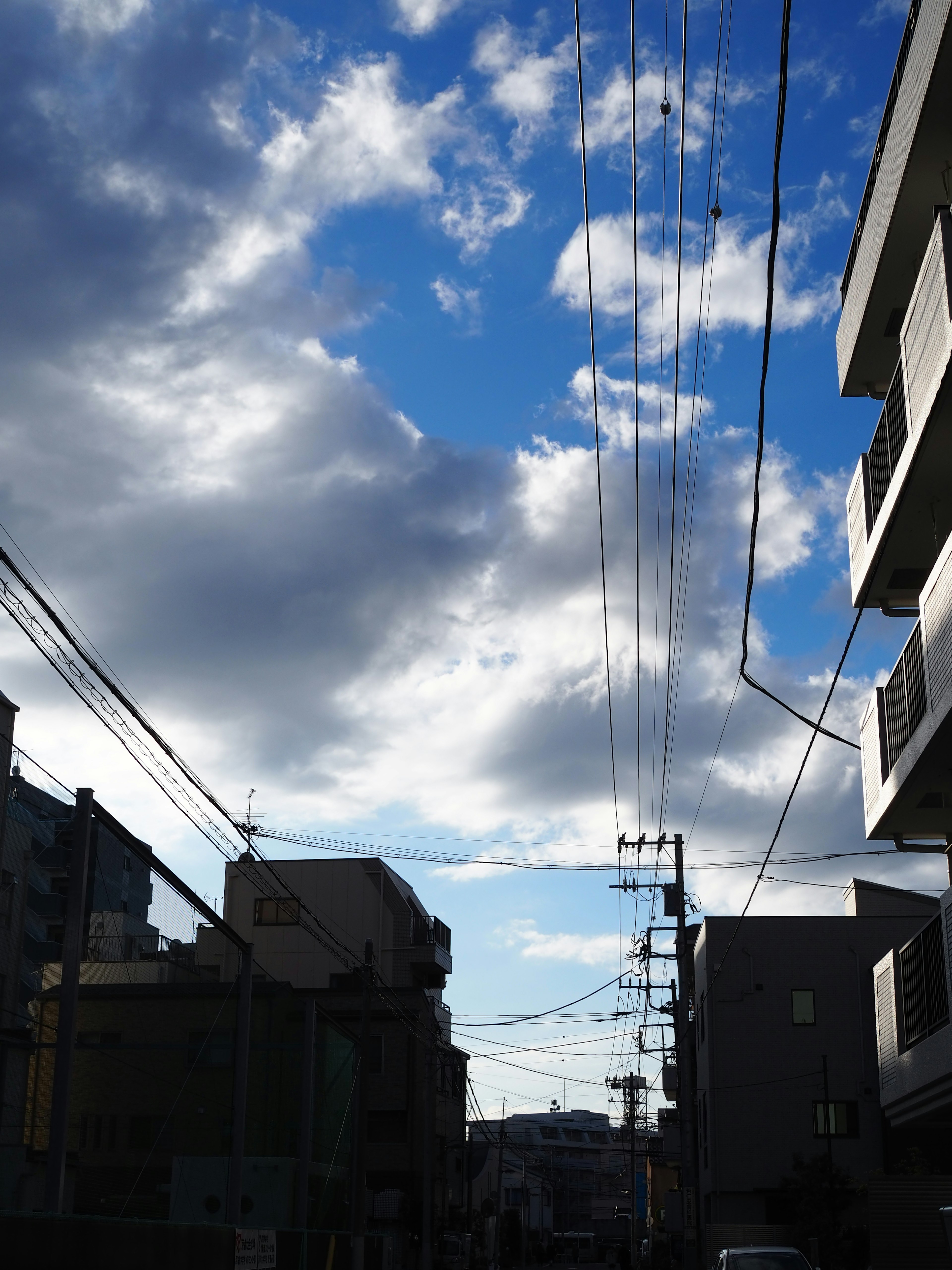 Urban street view with blue sky and clouds featuring utility poles and buildings