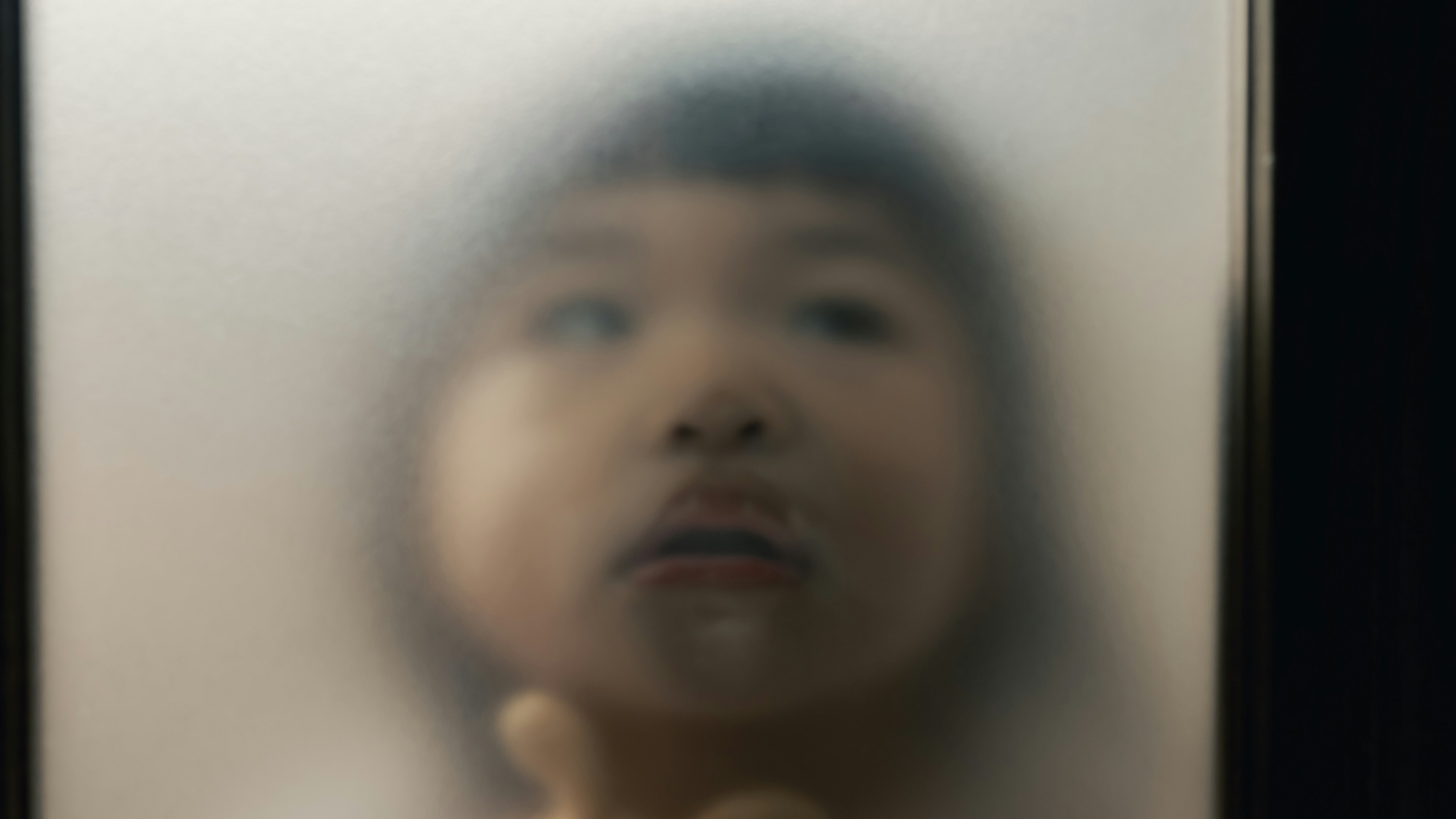 Child's face and hand seen through frosted glass