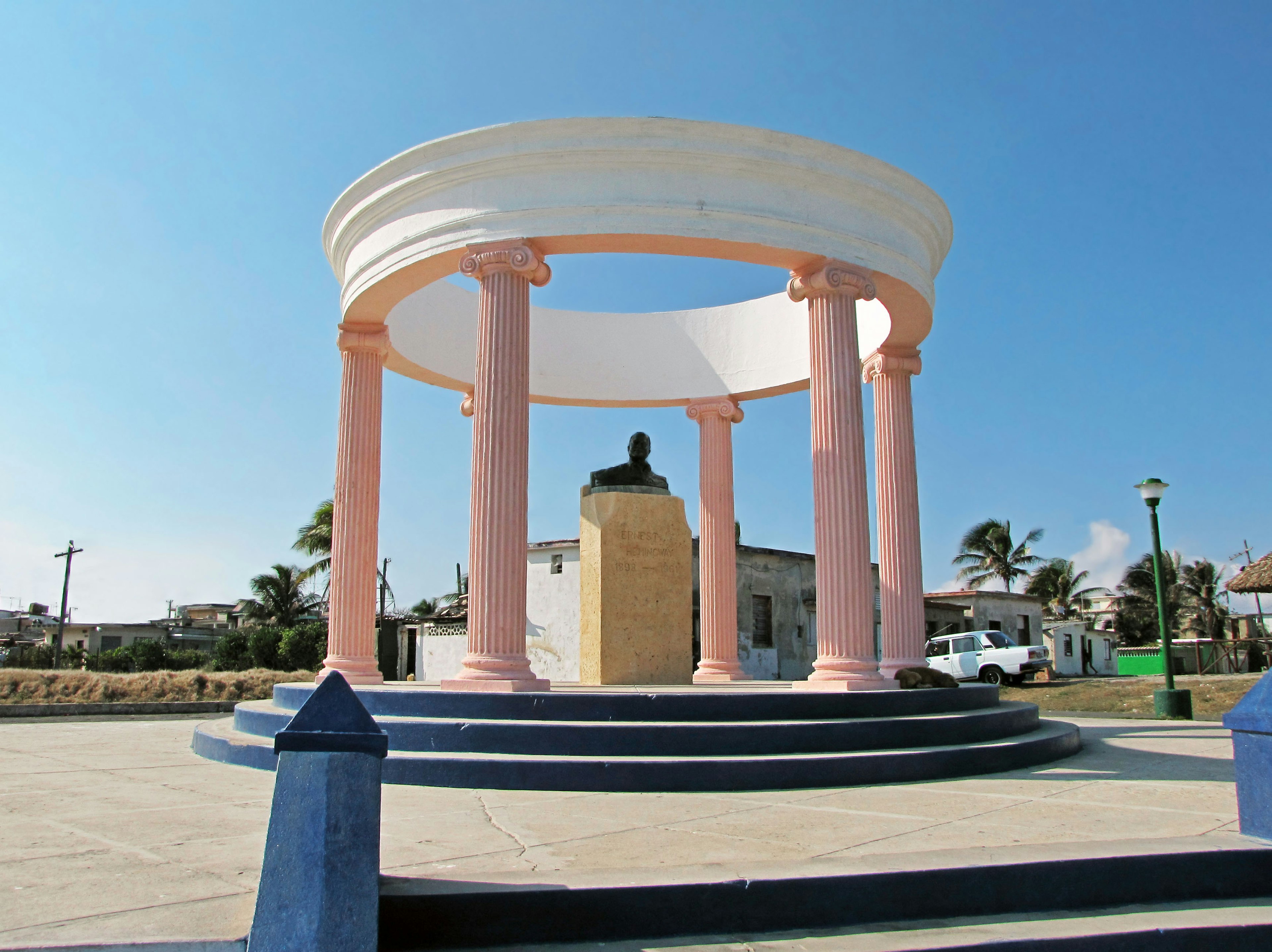 Monument circulaire avec des colonnes roses et une statue sous un ciel bleu