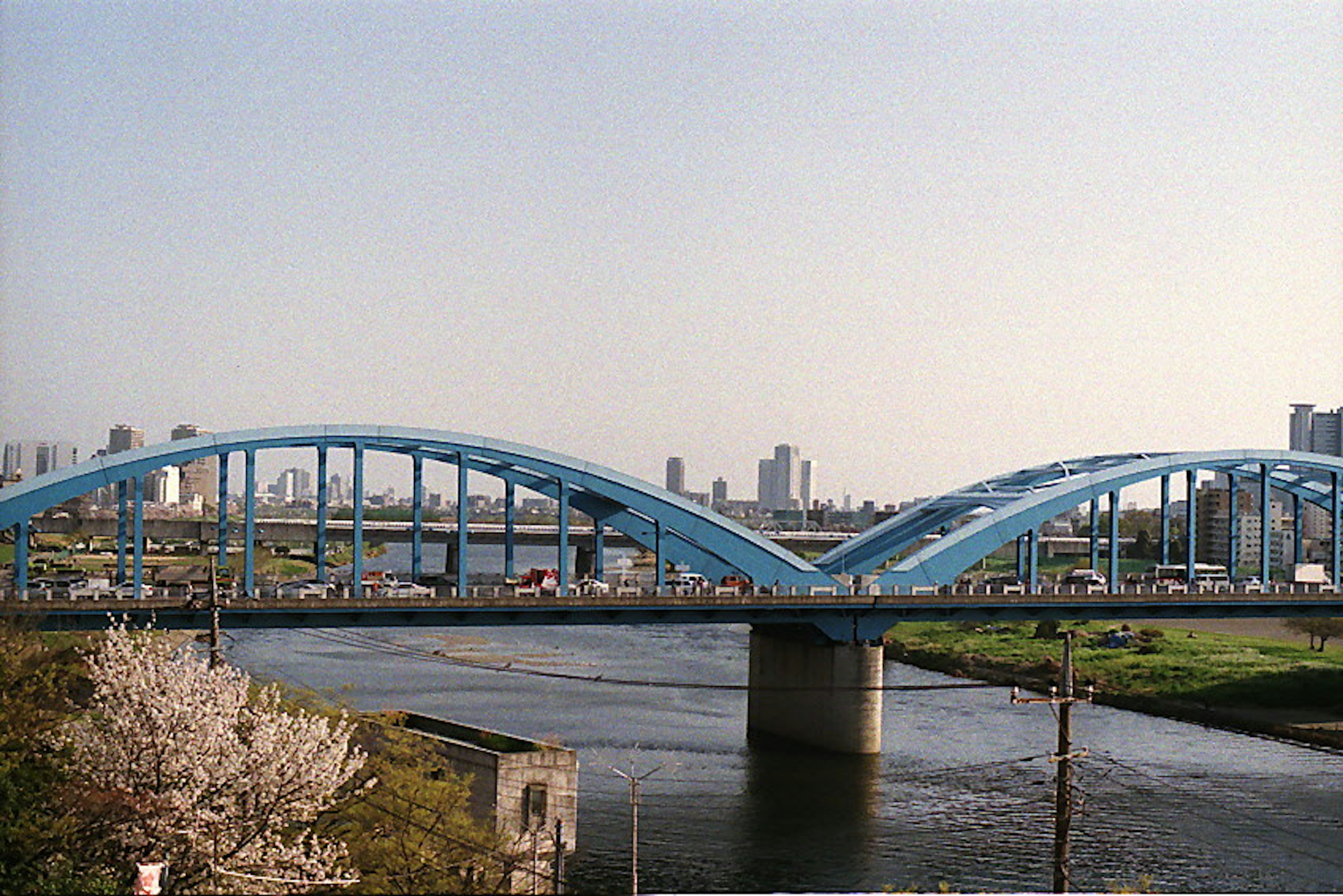 Blue arch bridge over a river with a city skyline