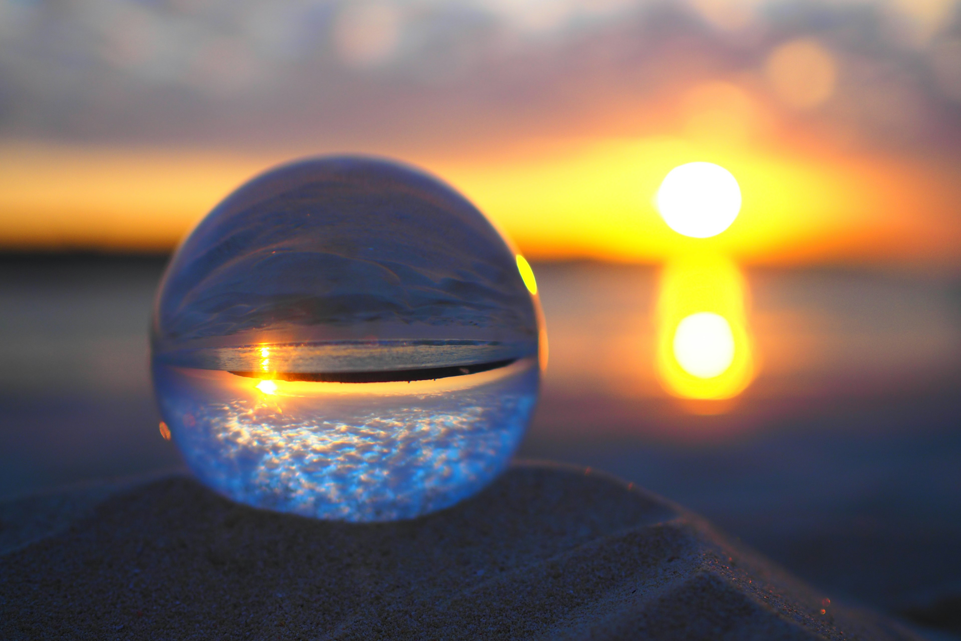 A crystal ball resting on the sand reflecting a beautiful sunset