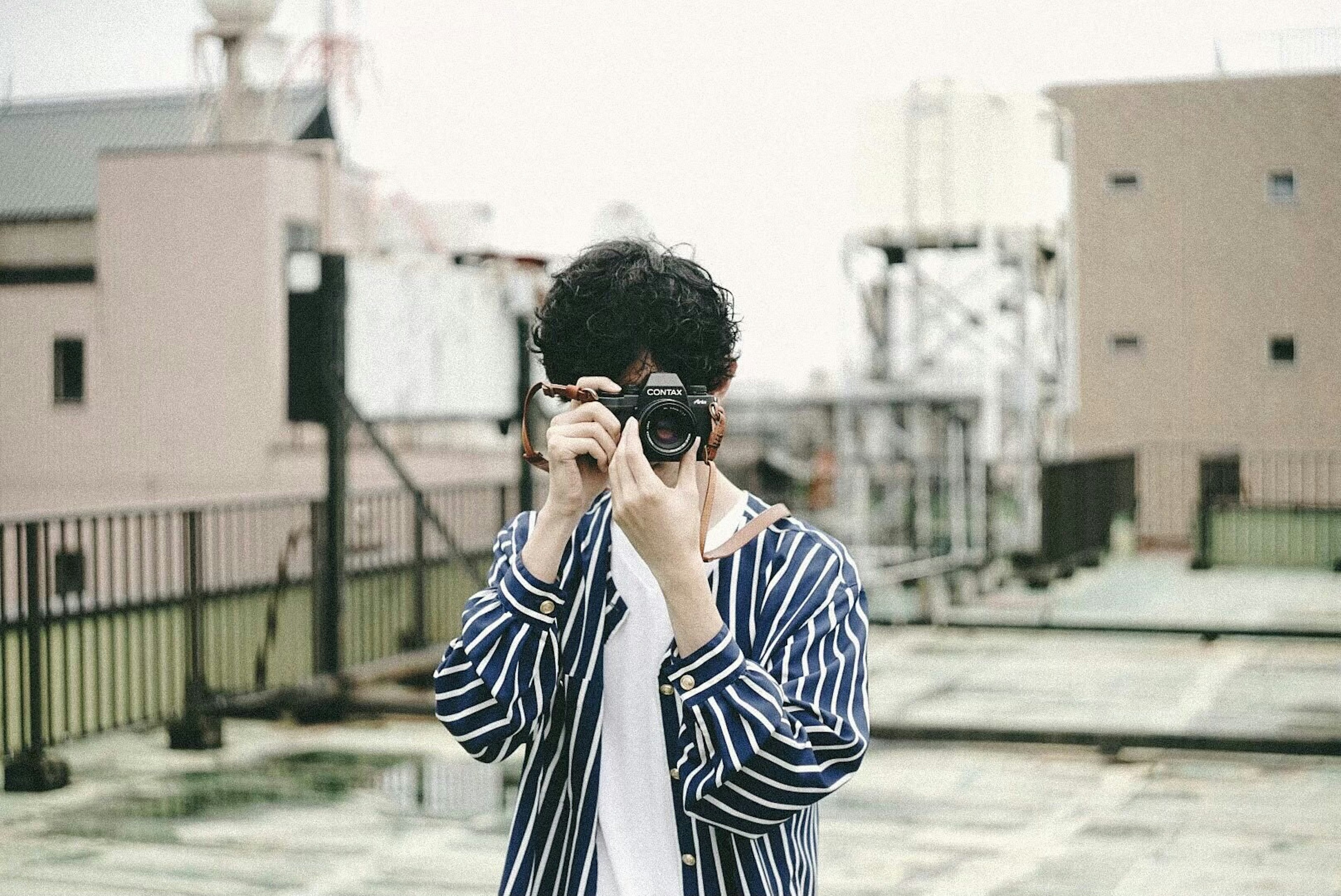 Young person holding a camera on a rooftop wearing a striped shirt