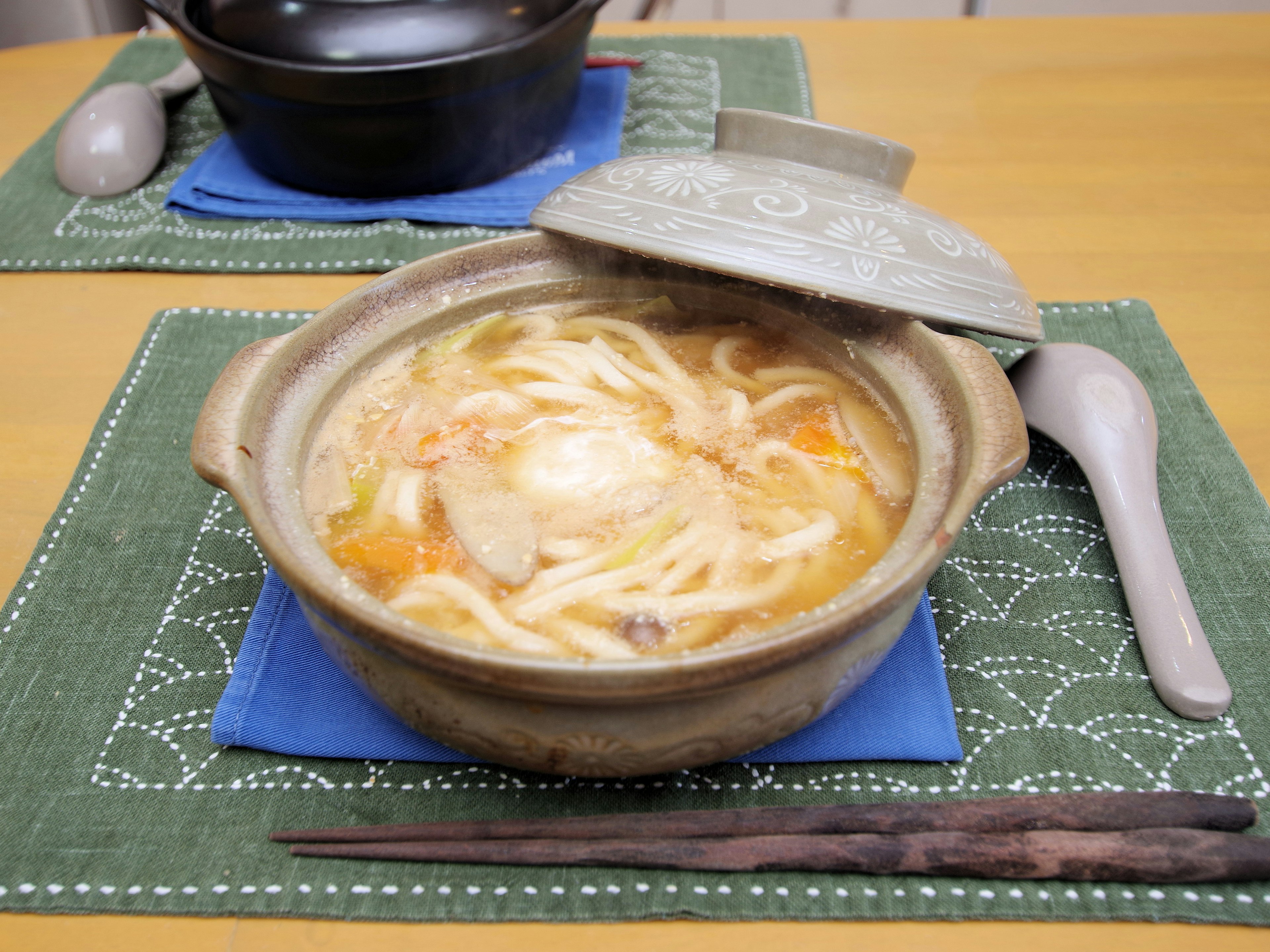 土鍋に盛られた温かいうどんと野菜のスープ