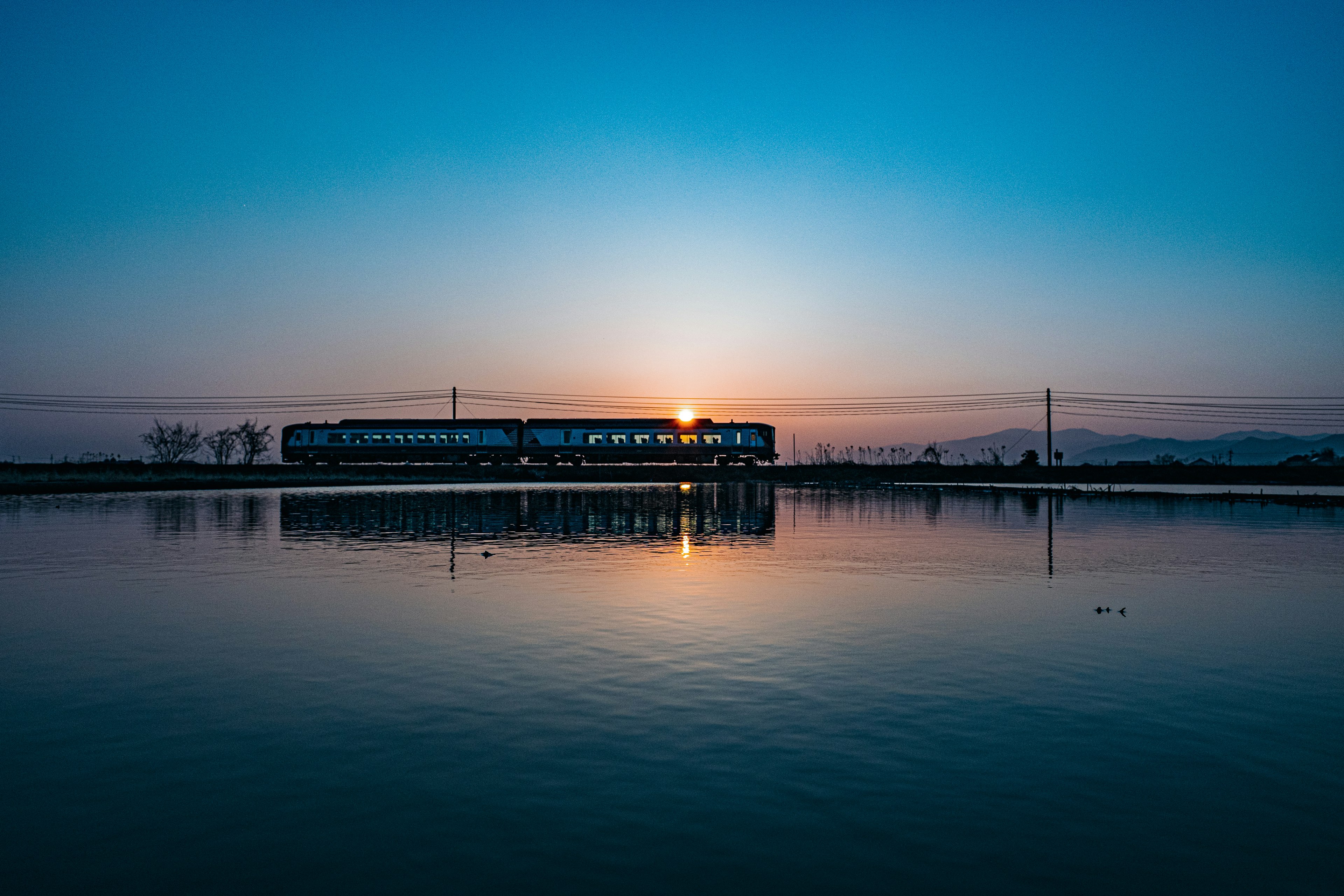 Silhouette di un treno che passa davanti a un tramonto riflesso sull'acqua