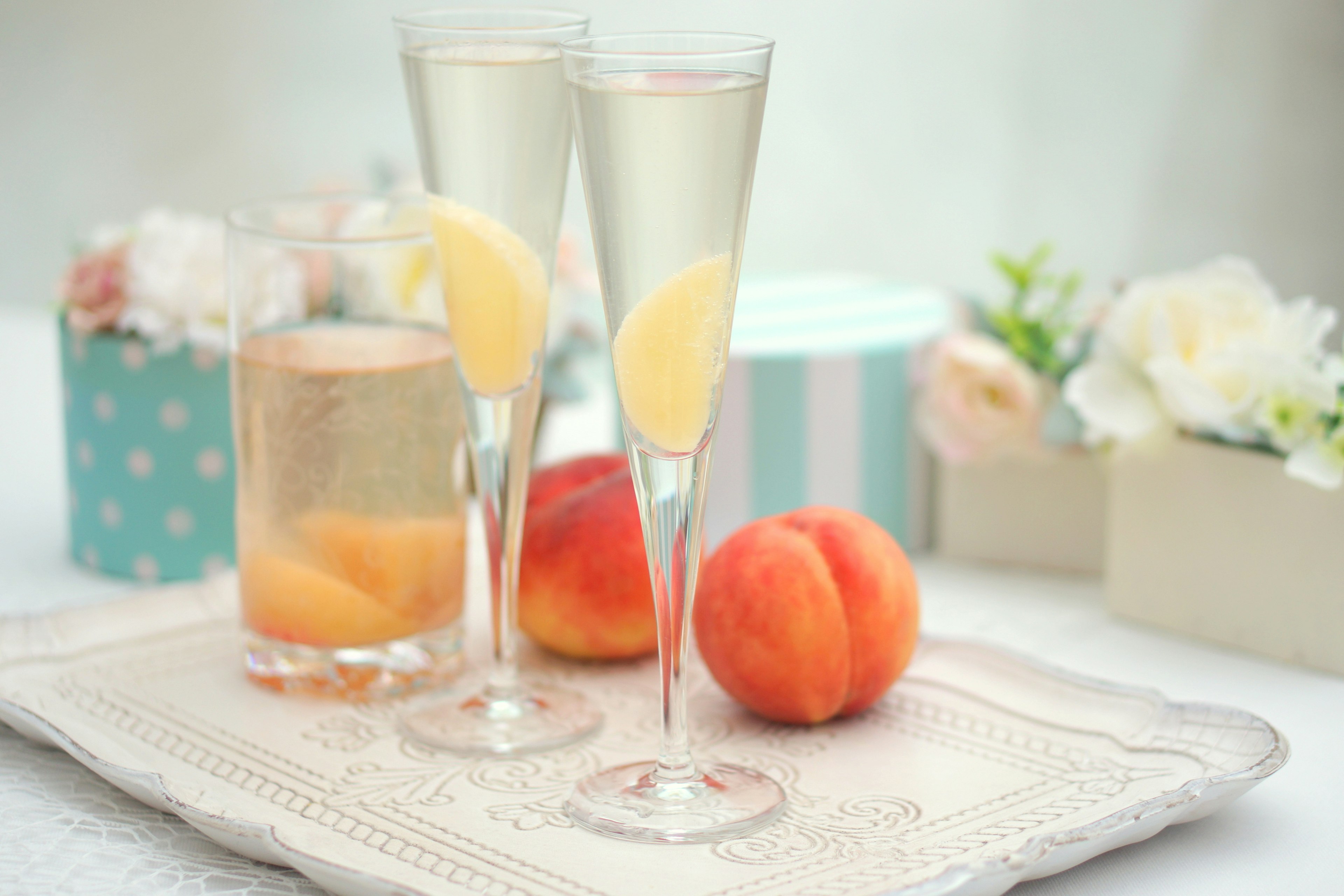 Two champagne glasses with lemon slices beside peaches on a decorative tray