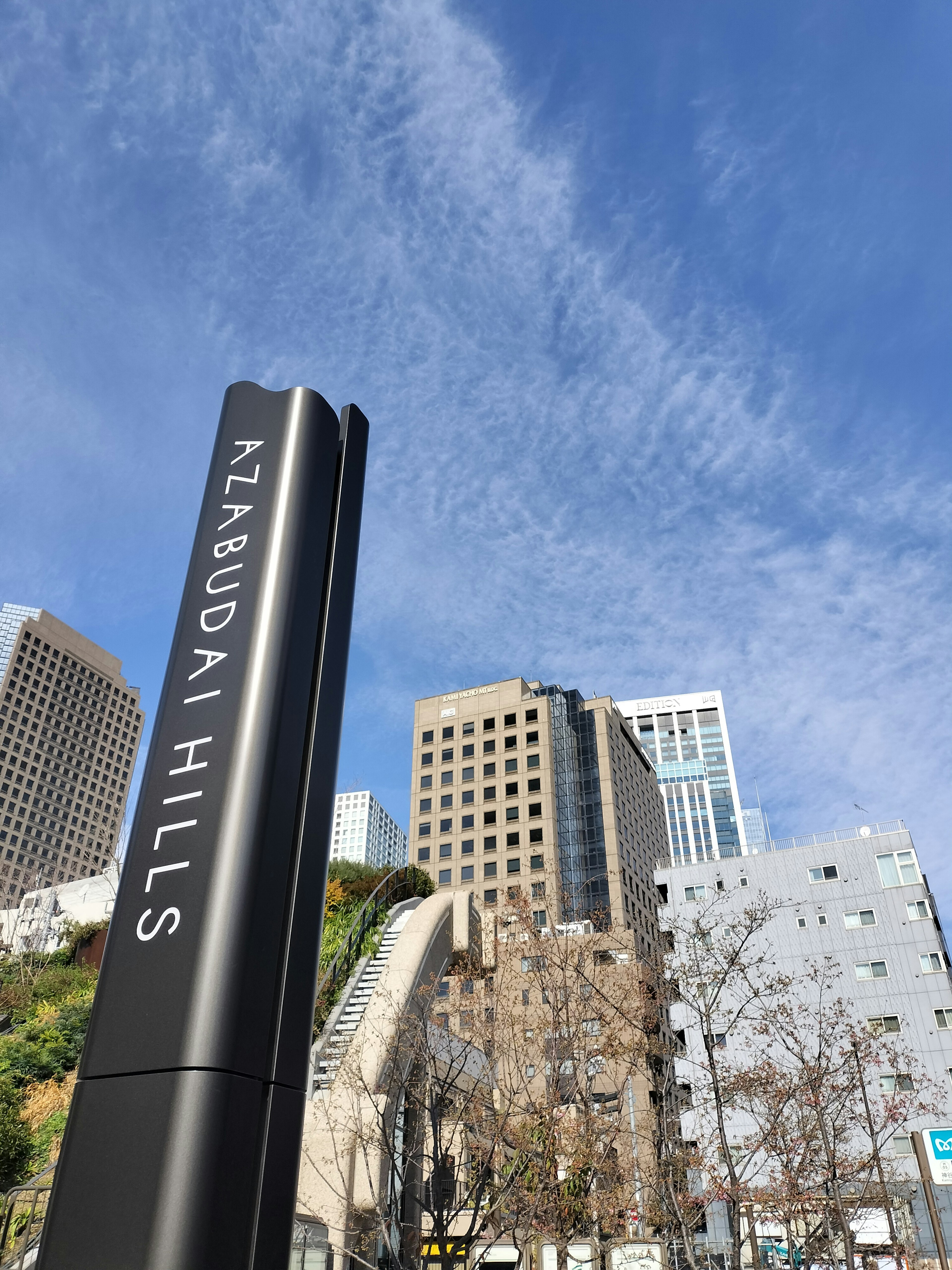 Sign for Azabudai Hills under a blue sky with skyscrapers