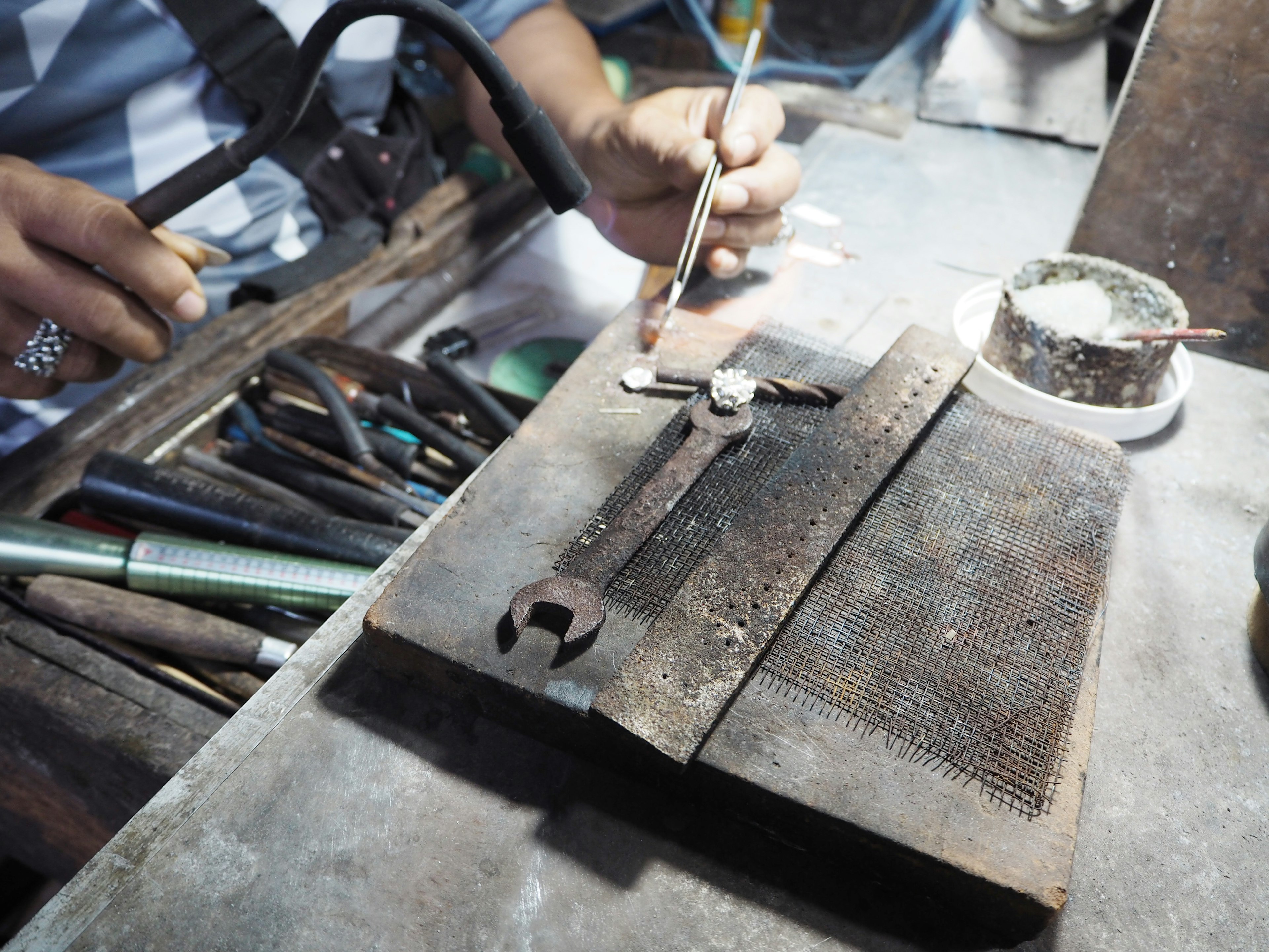 Hands using tools on a workbench with a metal measuring instrument