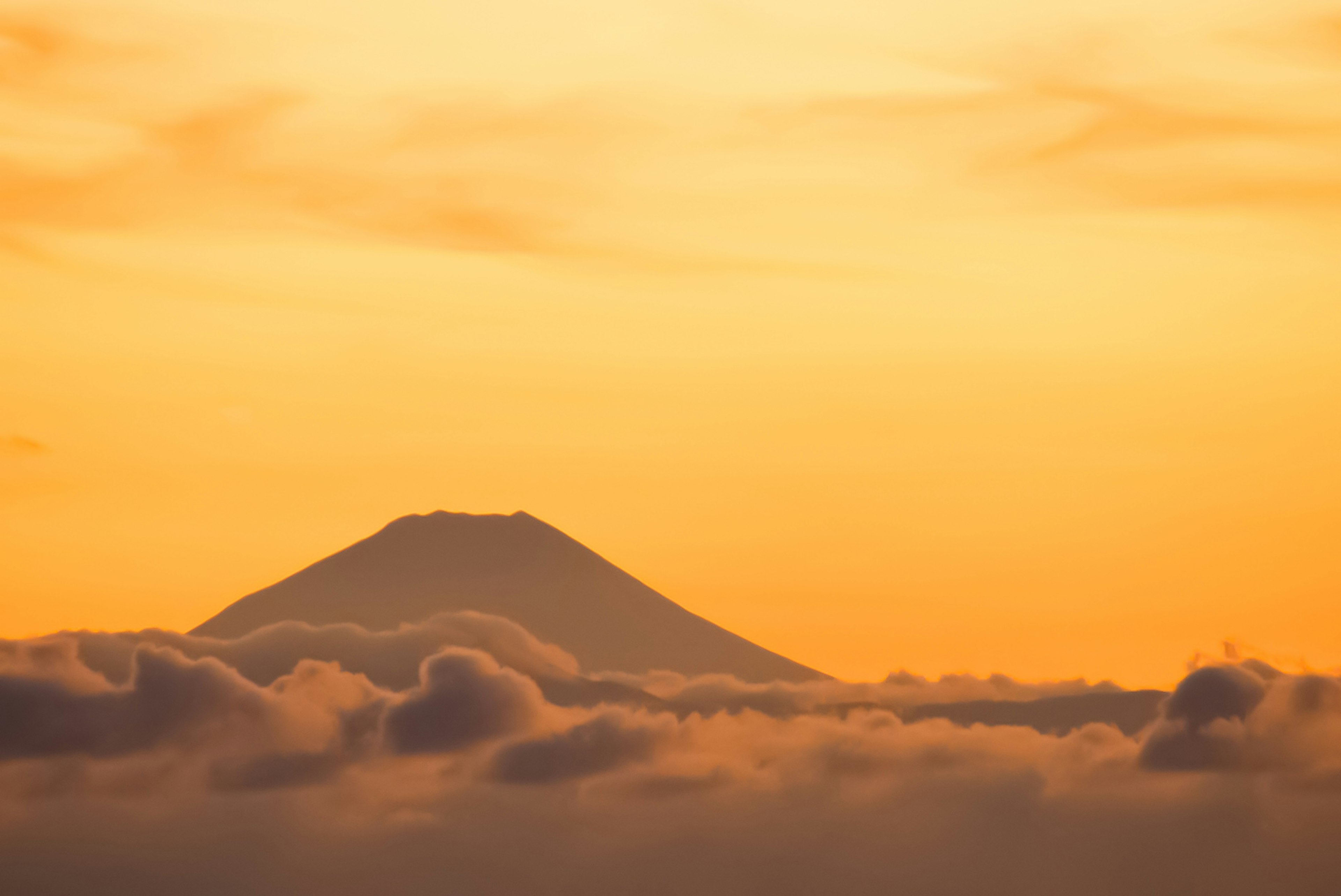Mount Fuji silhouetted against a golden sunset above the clouds