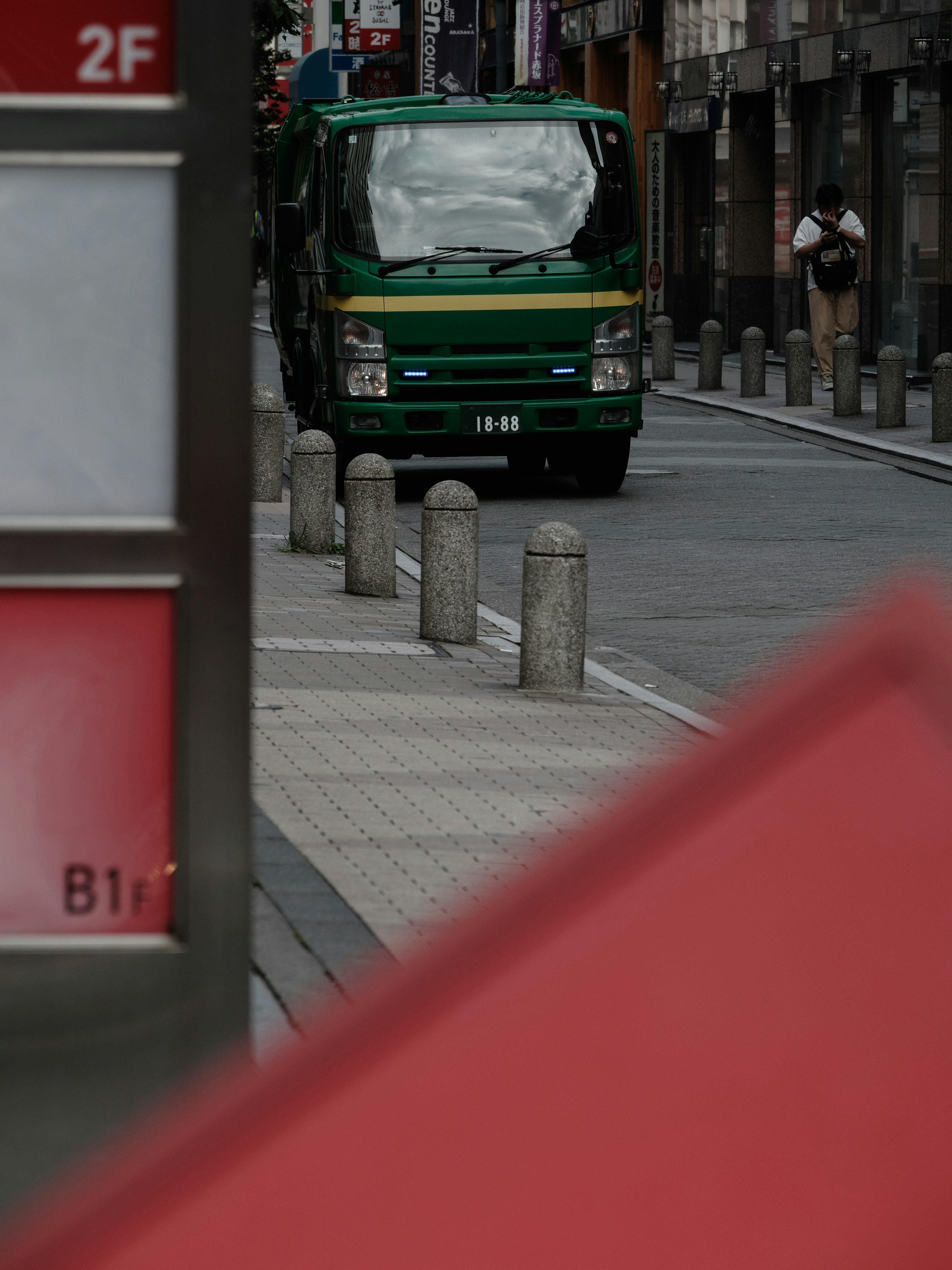 绿色货车在城市街道上行驶，旁边是混凝土路障