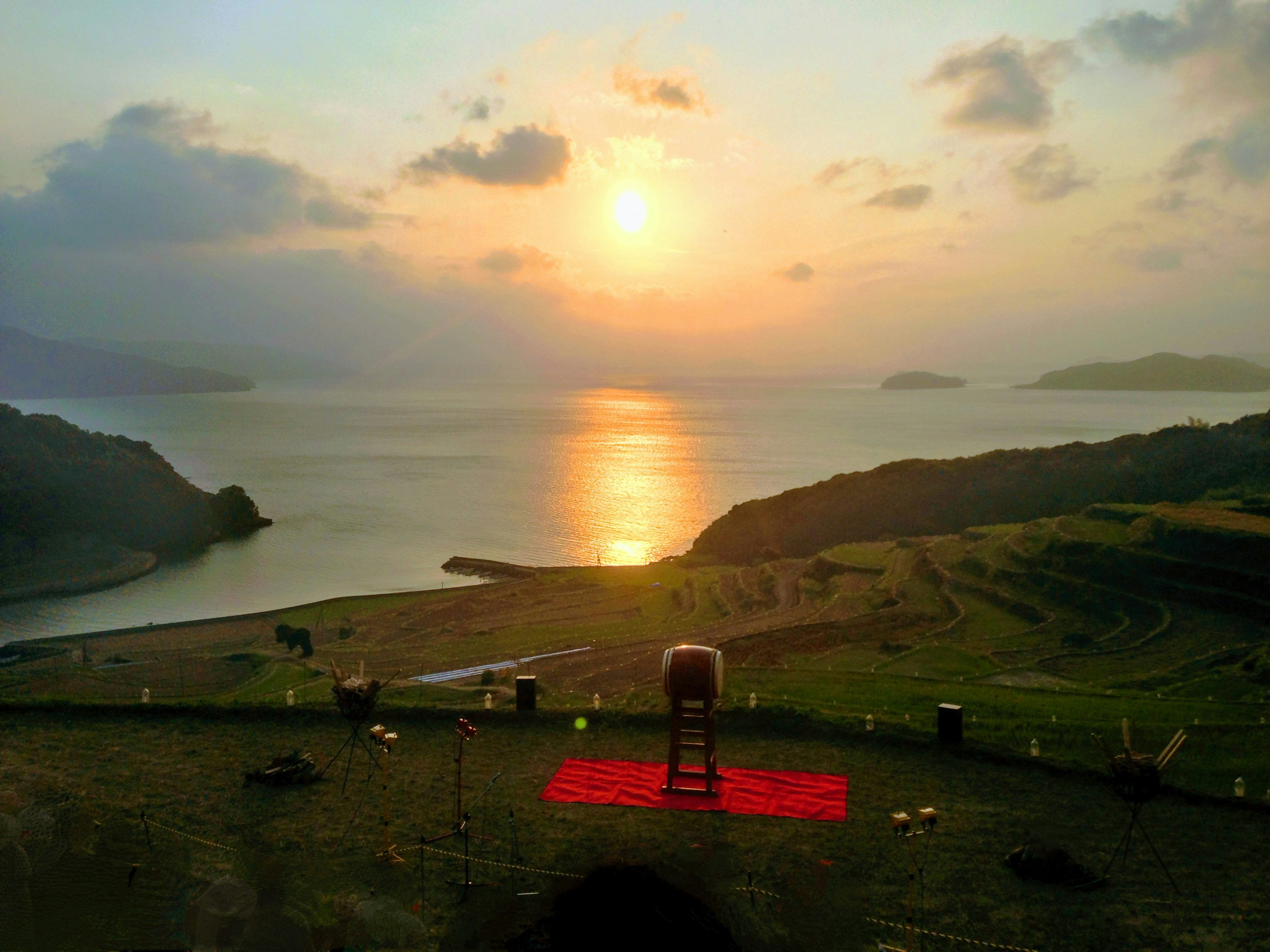 夕日が海に沈む風景と赤い絨毯がある丘の景色